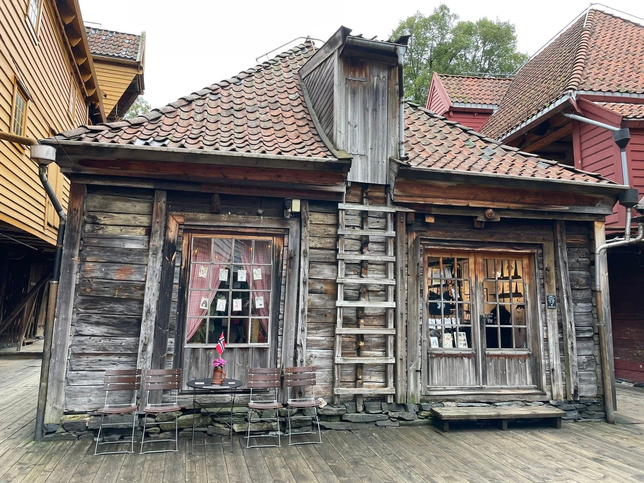 Weathered wooden storefront with chairs and a table holding a Norwegian flag on a boardwalk in Stavanger, Norway.