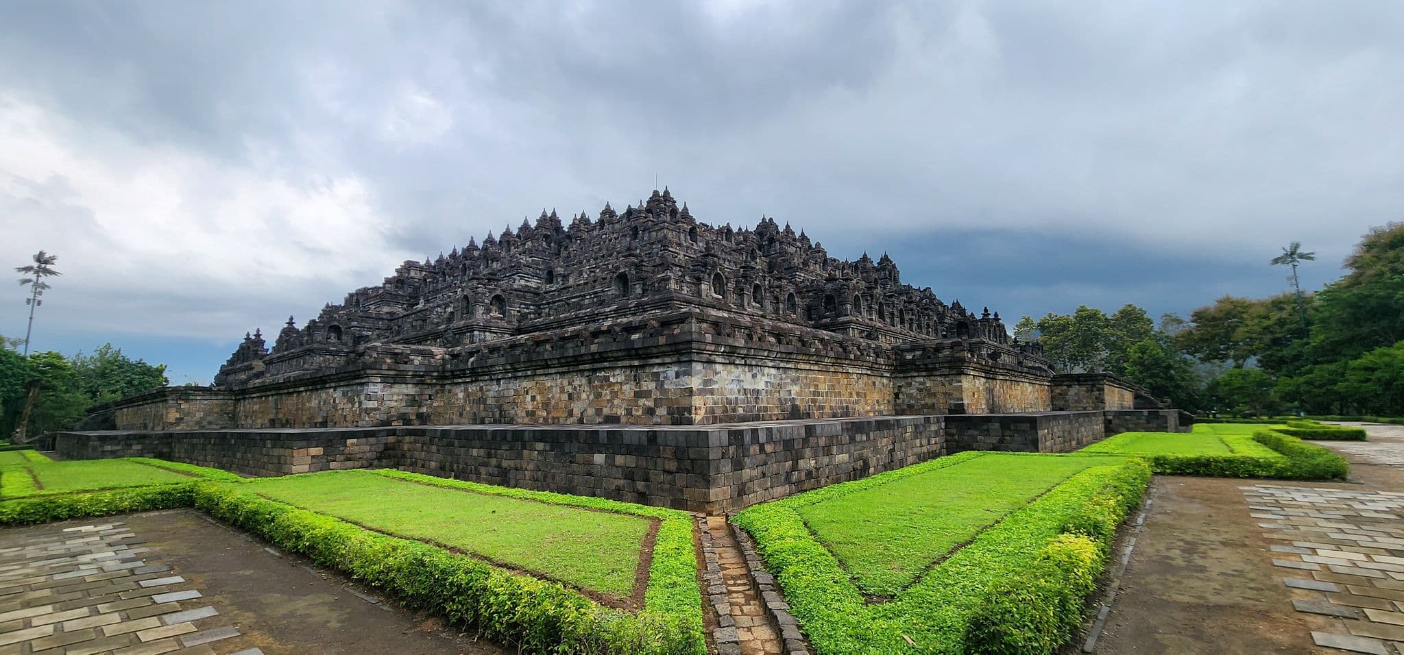 Borobudur Temple seen from a corner with layered stone terraces and manicured lawns in Magelang, Central Java, Indonesia.