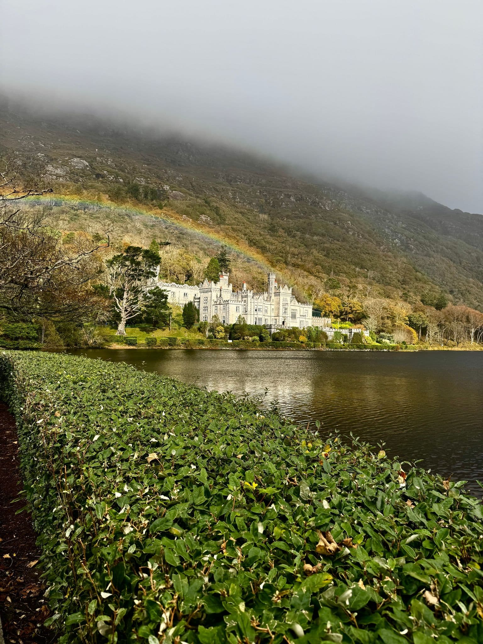 Kylemore Abbey with a rainbow arcing above it and reflecting in the lake, Connemara, Ireland.