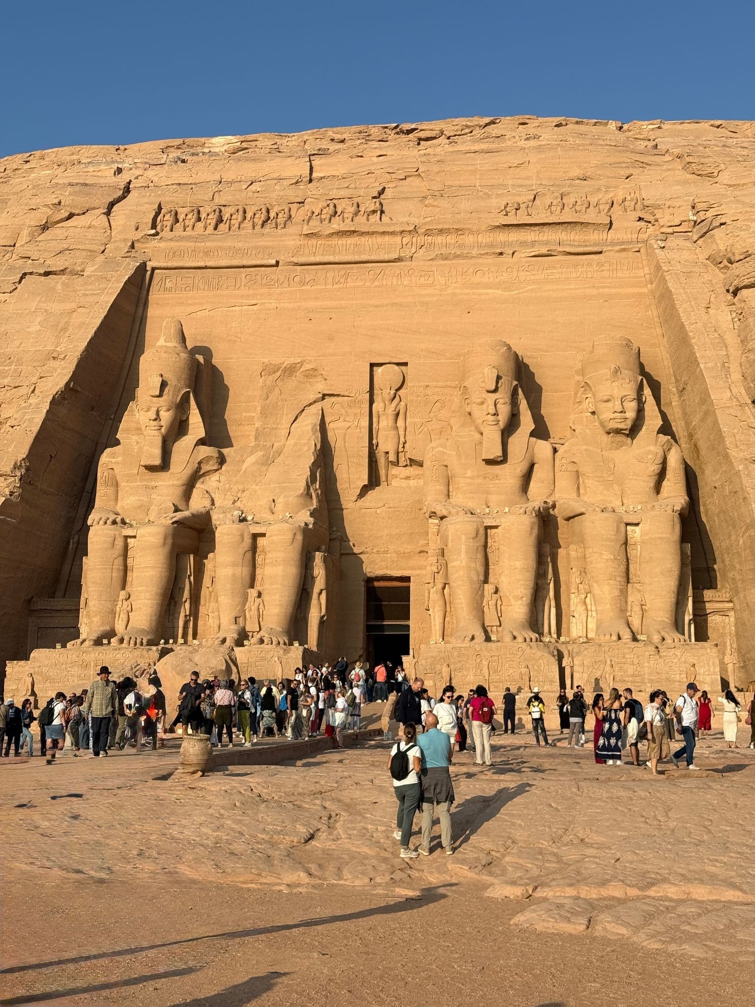 Great Temple of Ramesses II at Abu Simbel with giant seated statues and tourists gathered on the forecourt, Egypt.
