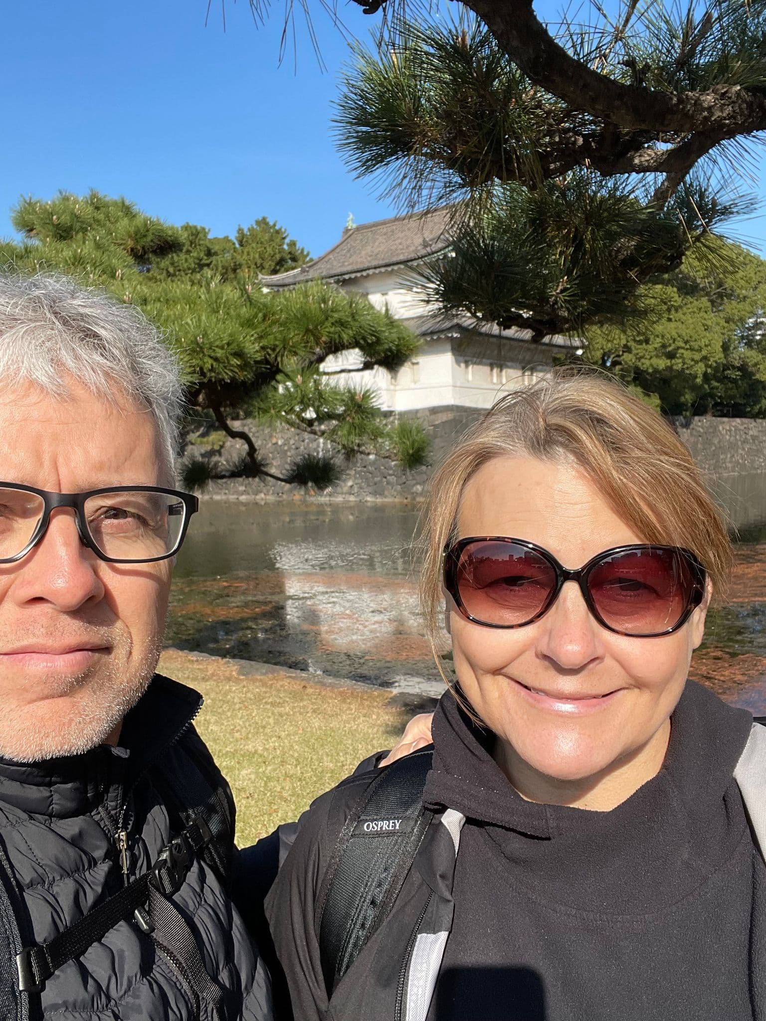 Imperial Palace building and moat with two travelers taking a selfie in Kokyo Gaien, Tokyo, Japan.