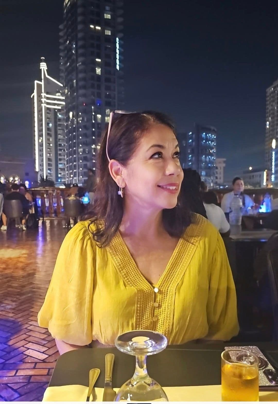 Woman at a rooftop restaurant looking up with illuminated Dubai skyline behind her, Dubai, United Arab Emirates.
