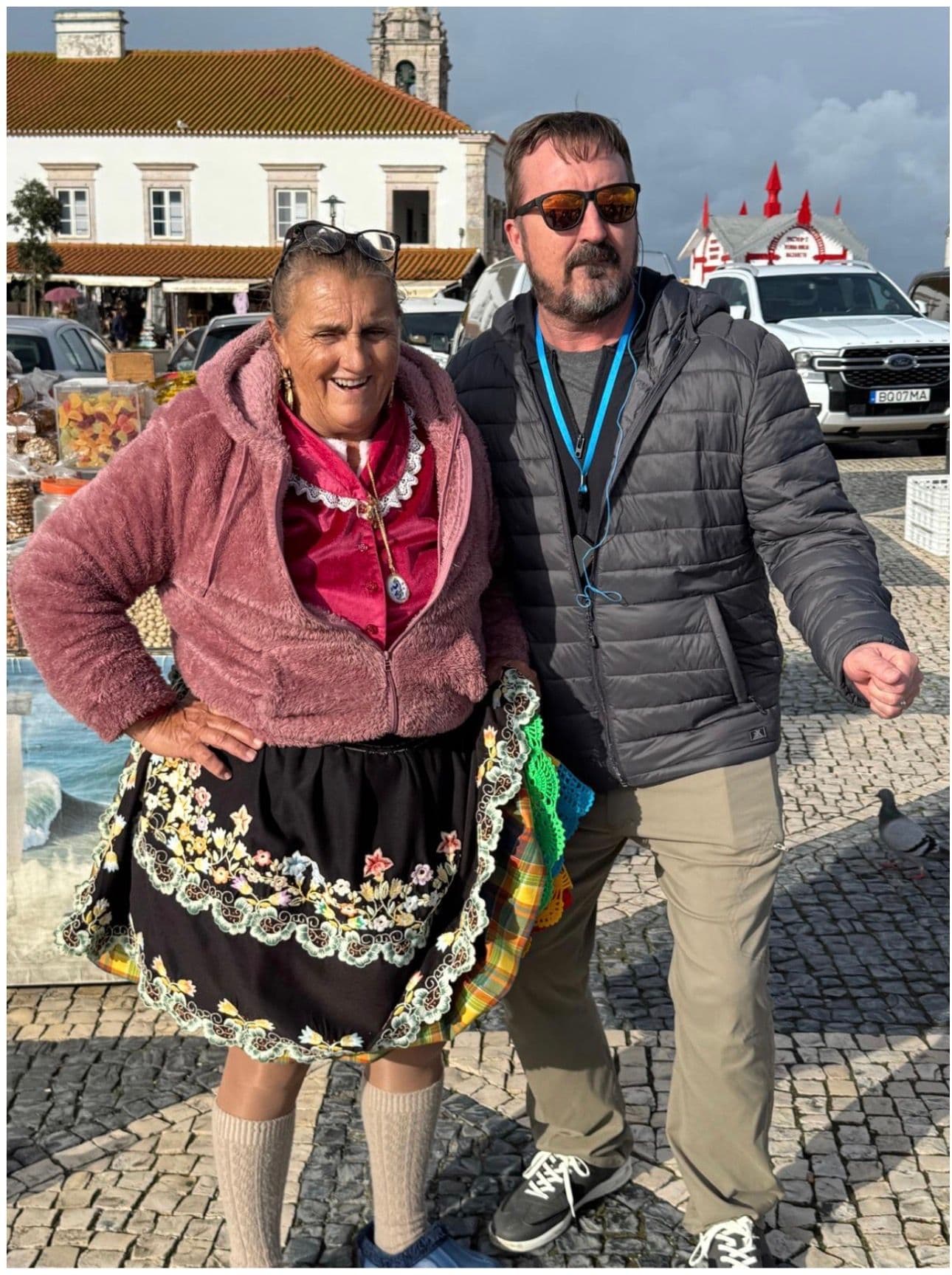 Local market vendor and a man posing together at an outdoor market square in Portugal.