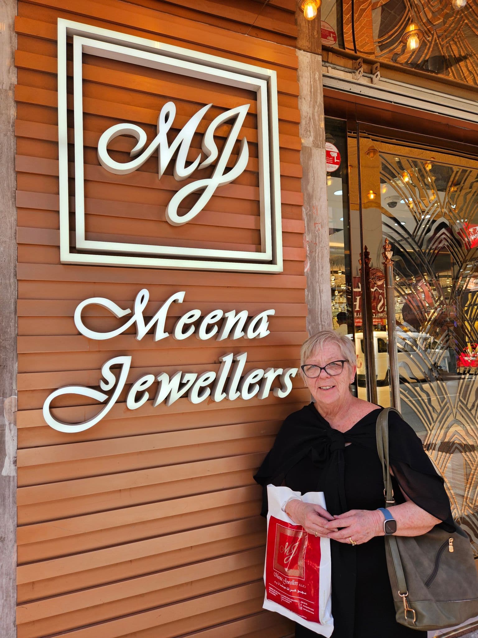 Meena Jewellers storefront sign with a woman standing beside it holding a shopping bag on a street in Dubai, United Arab Emirates.