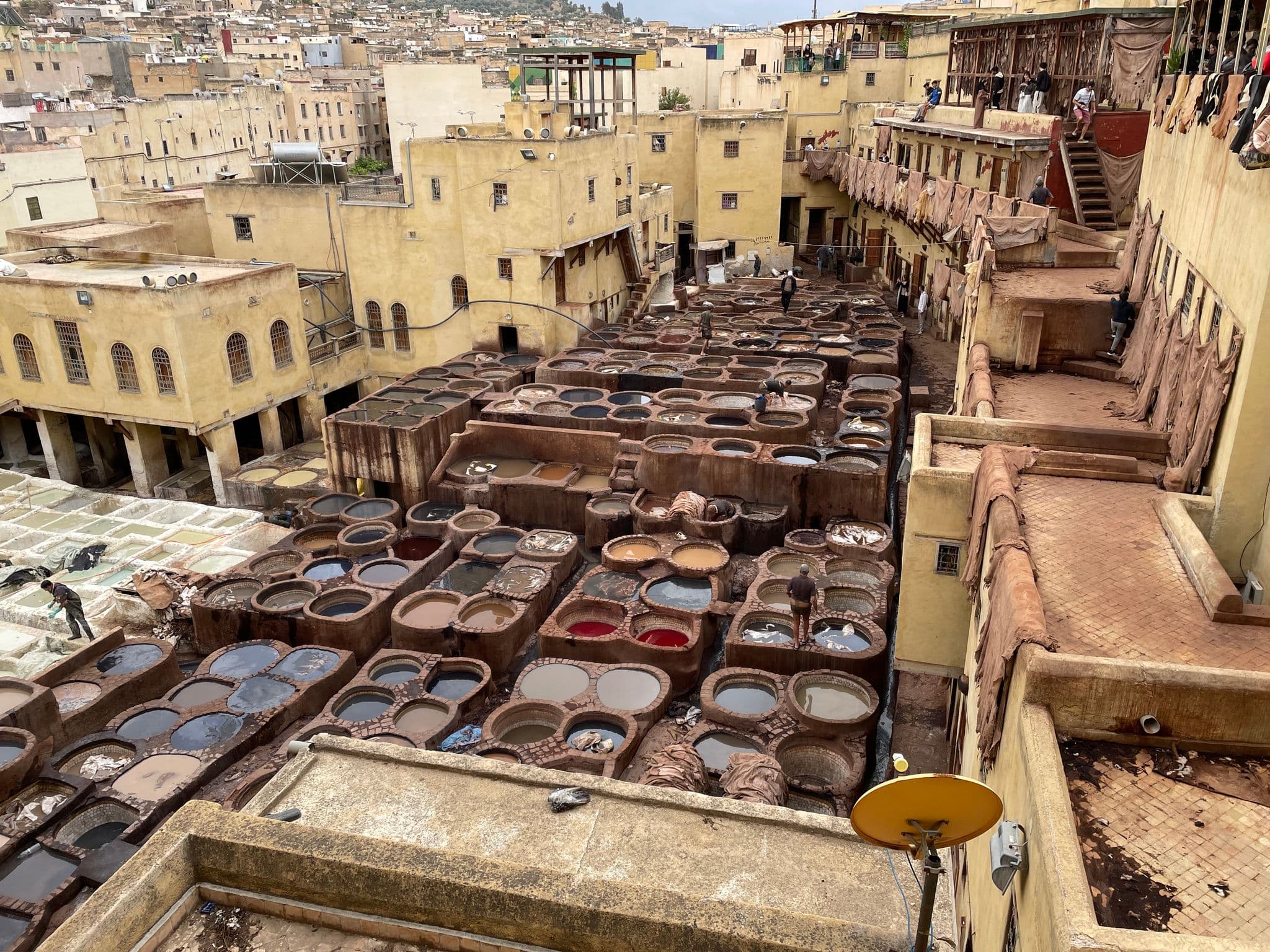 Rows of circular leather dye vats at a traditional tannery with workers and onlookers, Morocco.