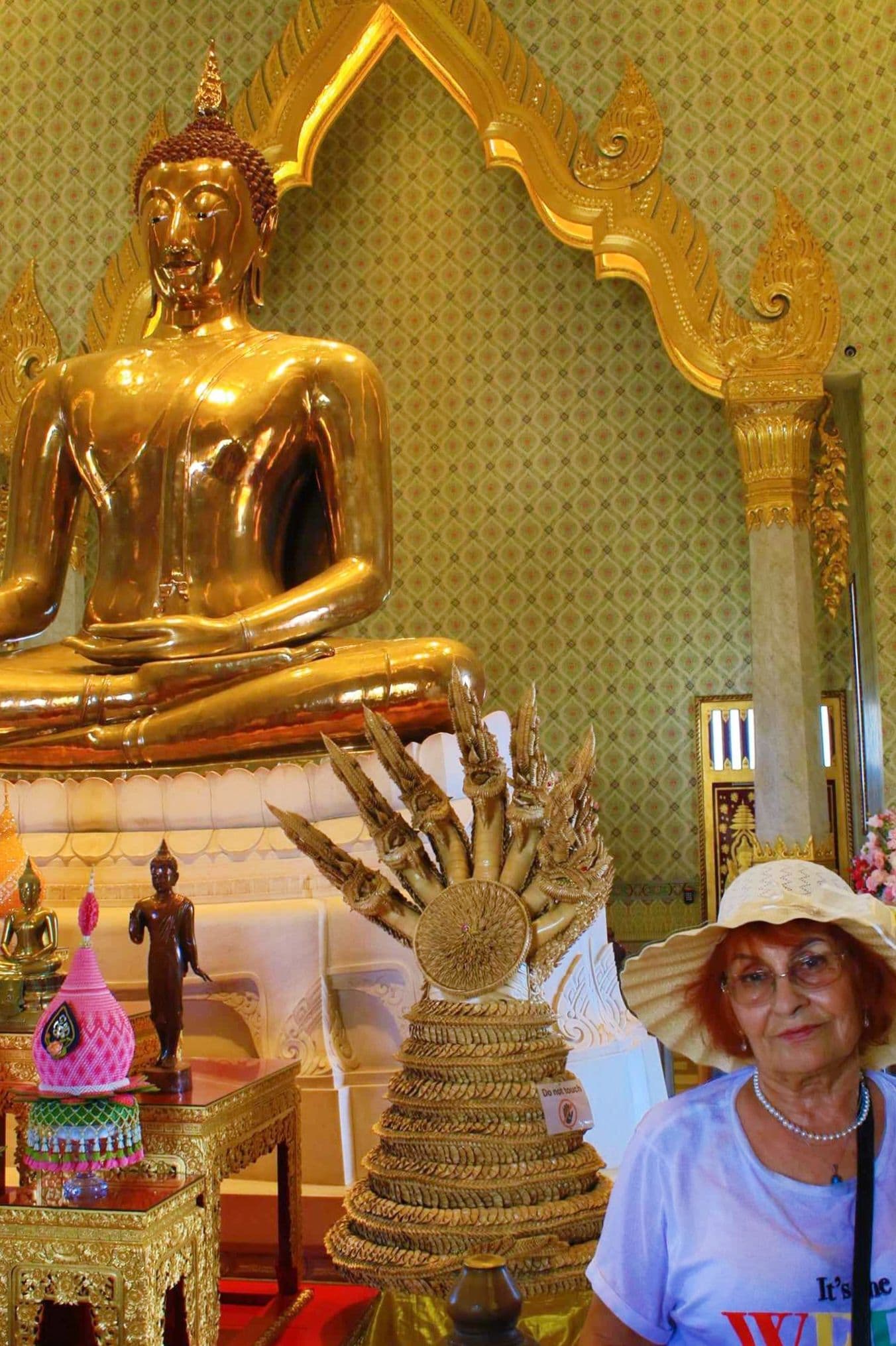 Seated Golden Buddha statue at Wat Traimit inside a Bangkok temple with a tourist wearing a sun hat at the right.