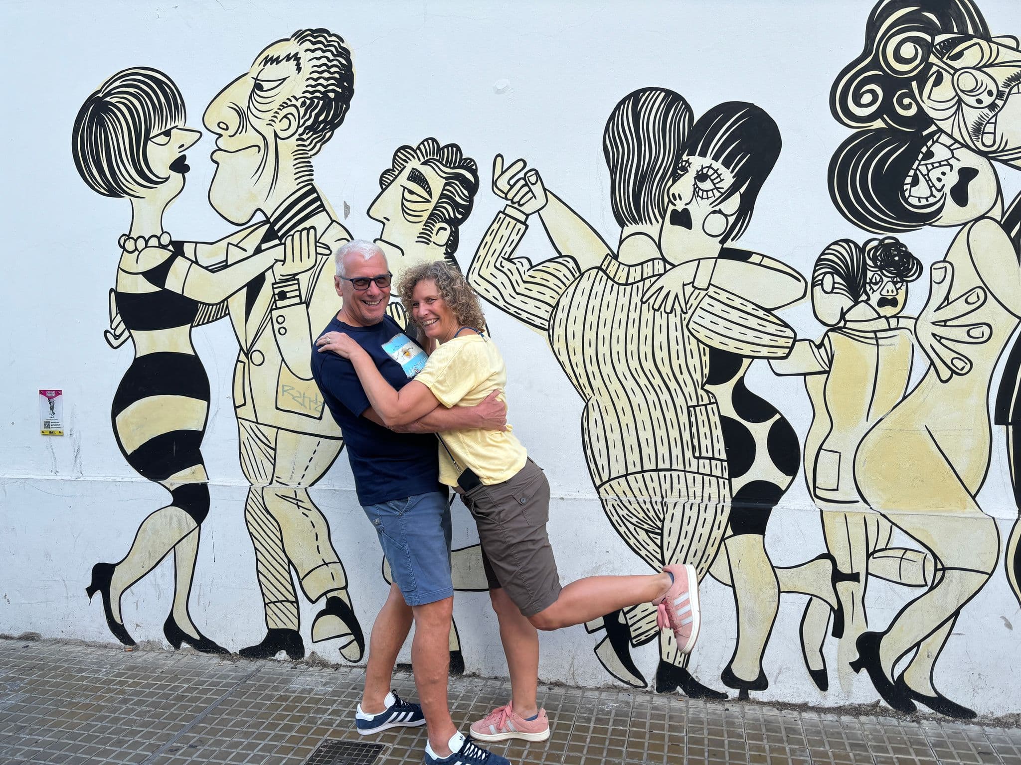 Couple embracing and posing with one leg lifted in front of a tango-themed street mural, Buenos Aires, Argentina.