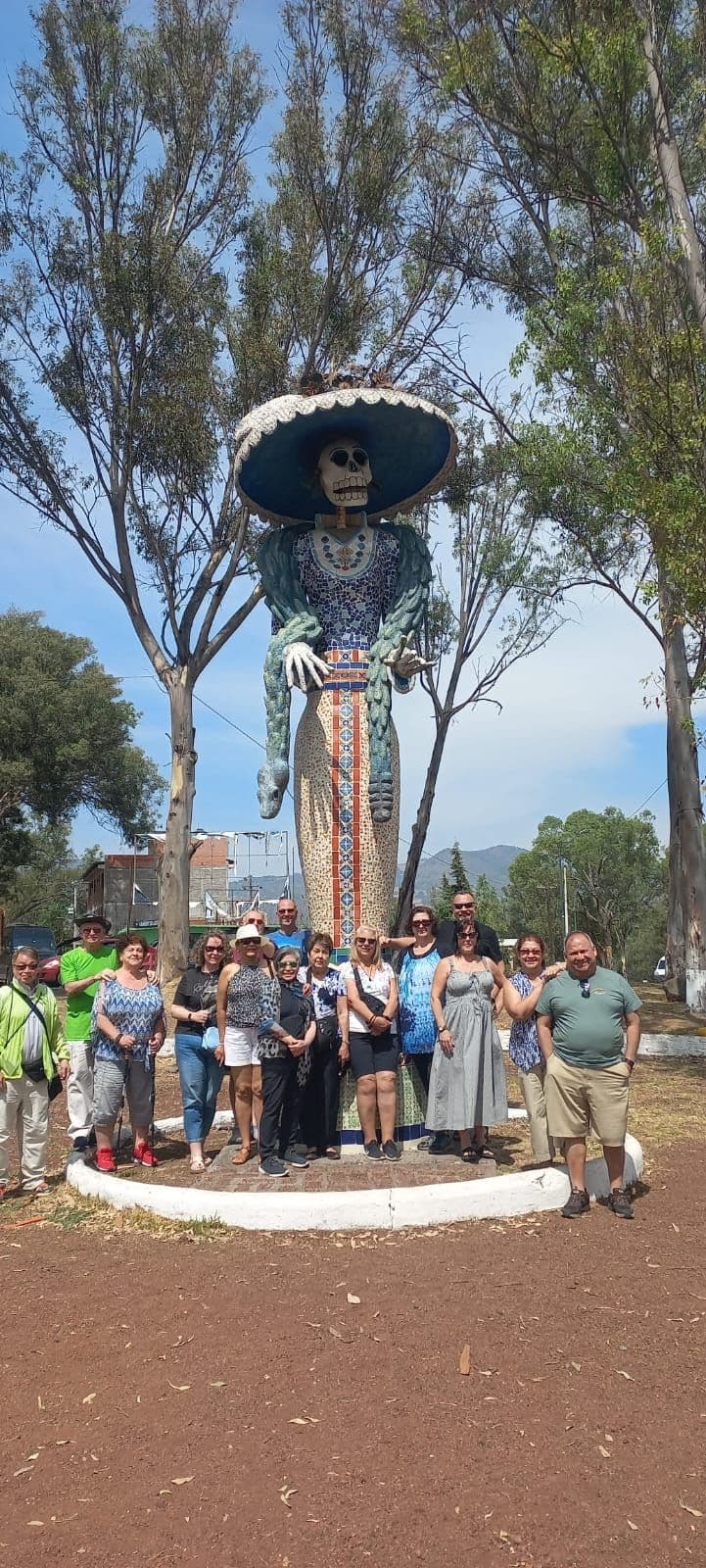 La Catrina statue towering behind a group of travelers posing for a tour photo in Mexico.