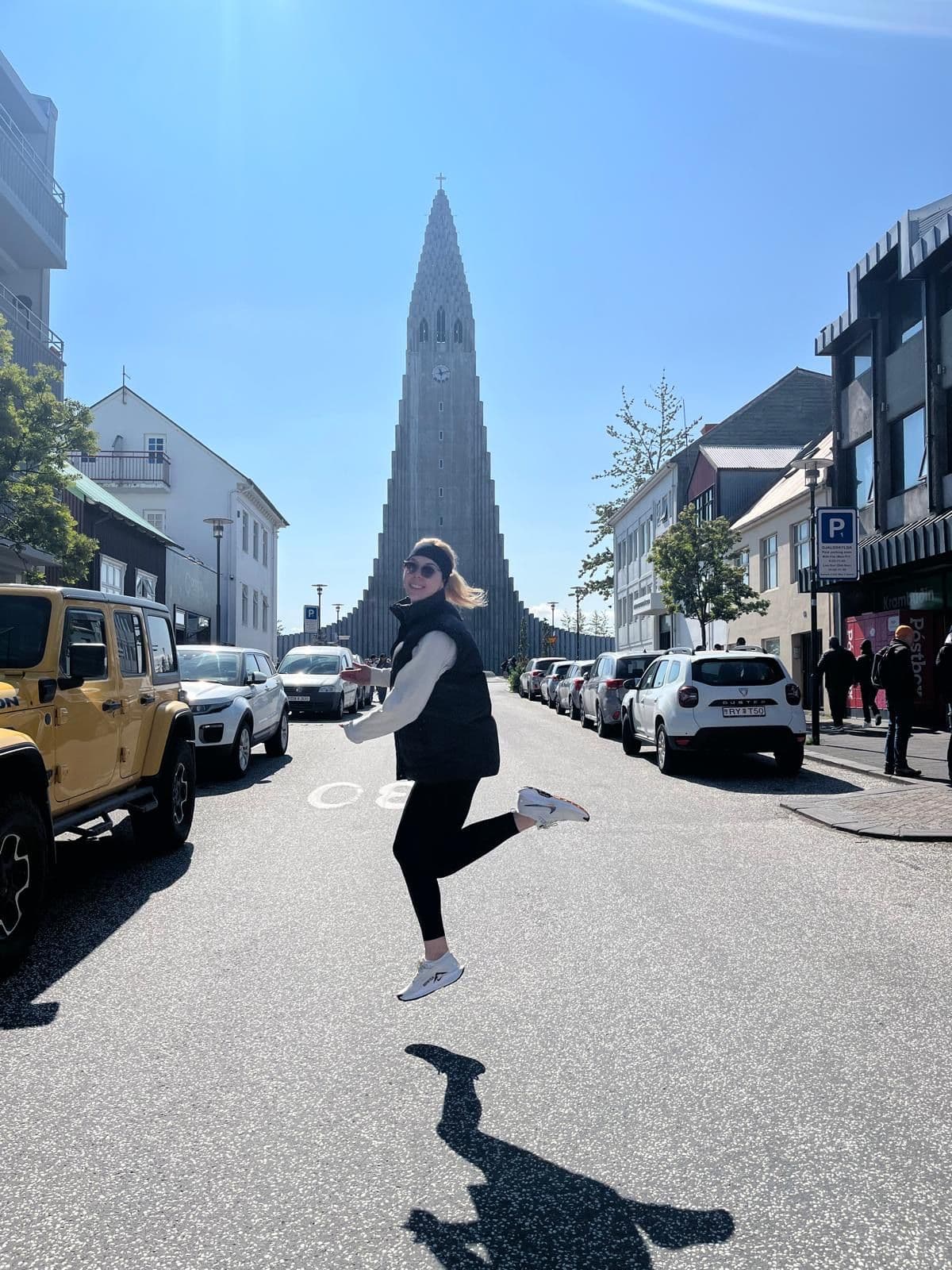 Hallgrímskirkja church with a person jumping mid-air on a sunlit street in Reykjavík, Iceland.