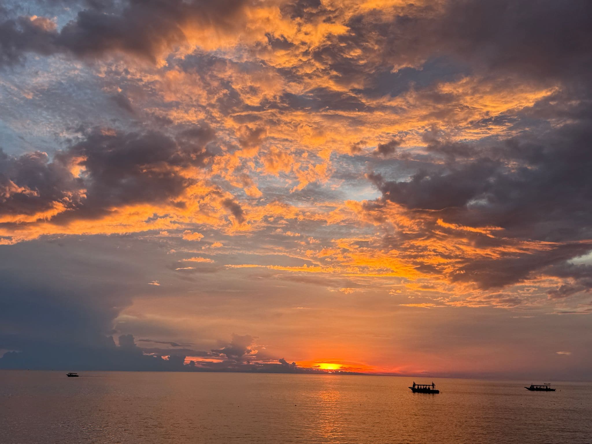 Tonle Sap Lake at sunset with an orange sky and silhouetted boats on the water, Cambodia.