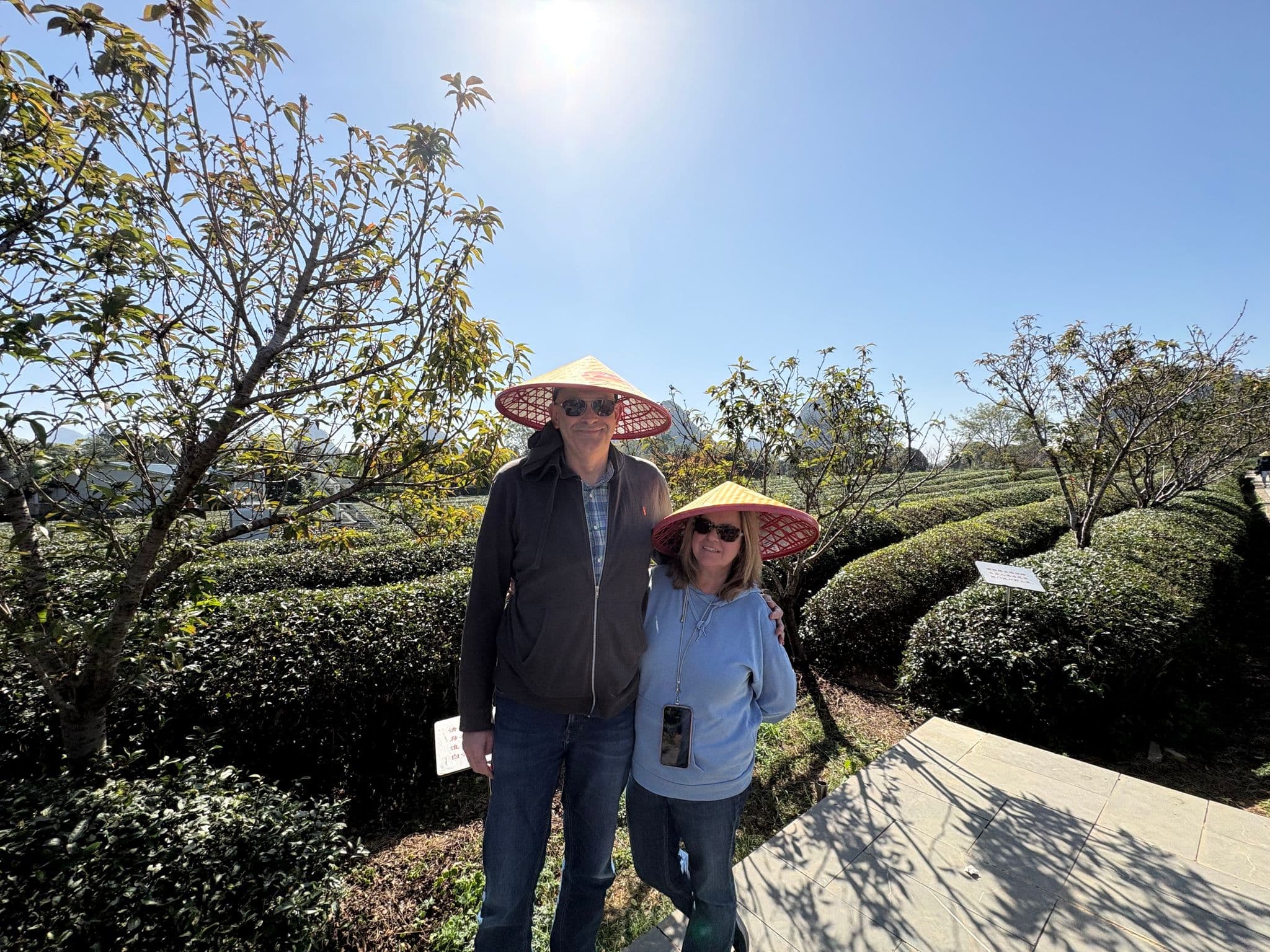Two travelers wearing conical hats posing among tea bushes at a plantation in Guilin, China.