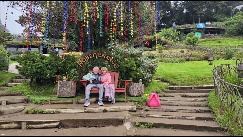 Hobbitenango hillside bench with two travelers sitting under colorful hanging ornaments, Antigua, Guatemala.