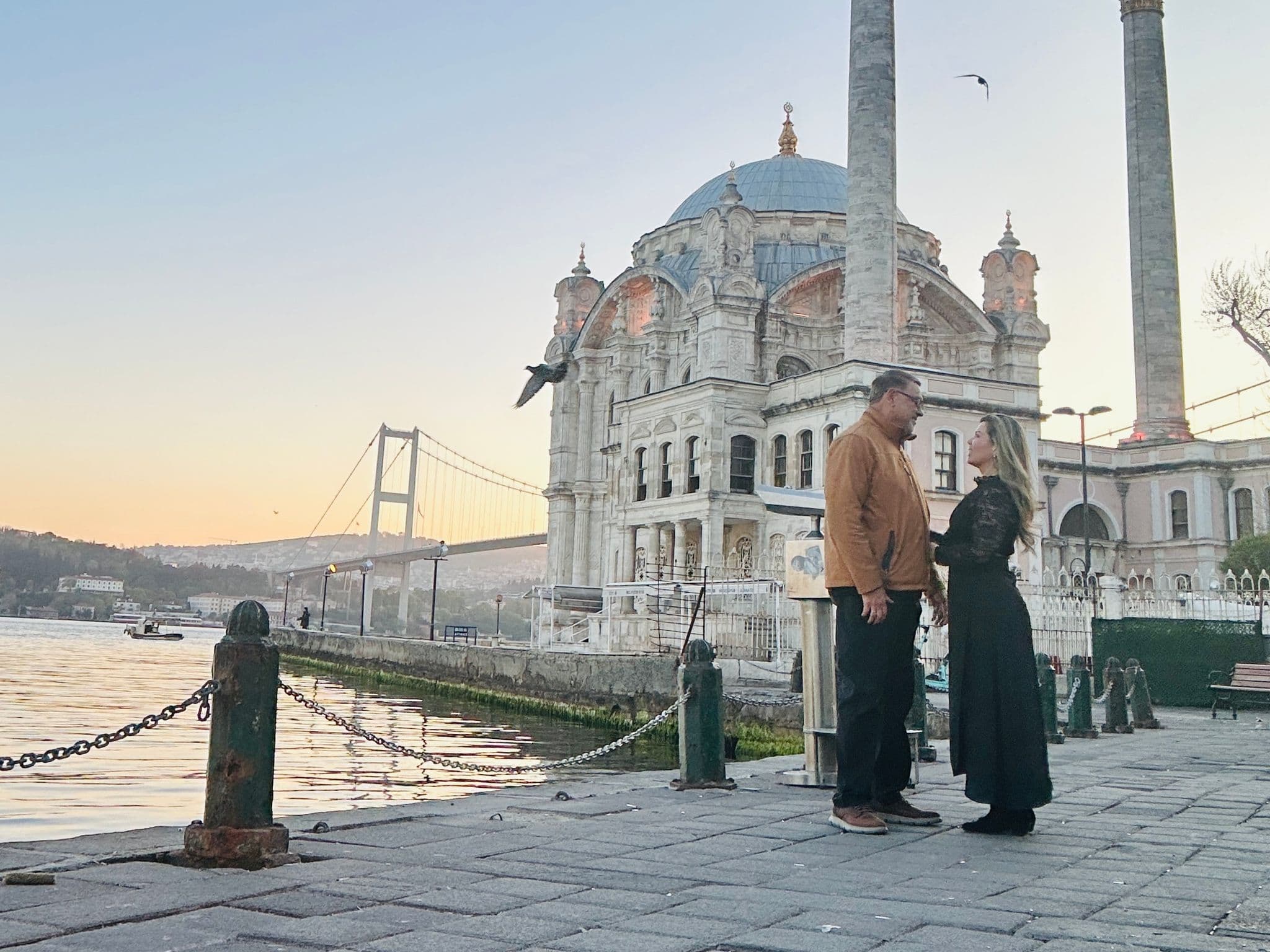 Ortaköy Mosque beside the Bosphorus at sunset with a couple standing on the waterfront in Istanbul, Turkey.