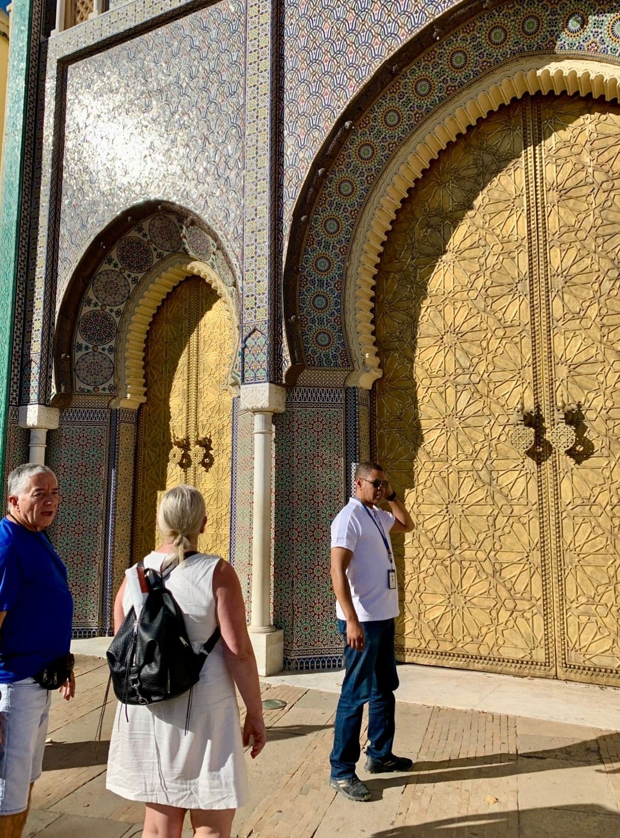 Ornate golden palace doors at the Royal Palace gates, Fez, Morocco, with tourists standing and looking at the entrance.