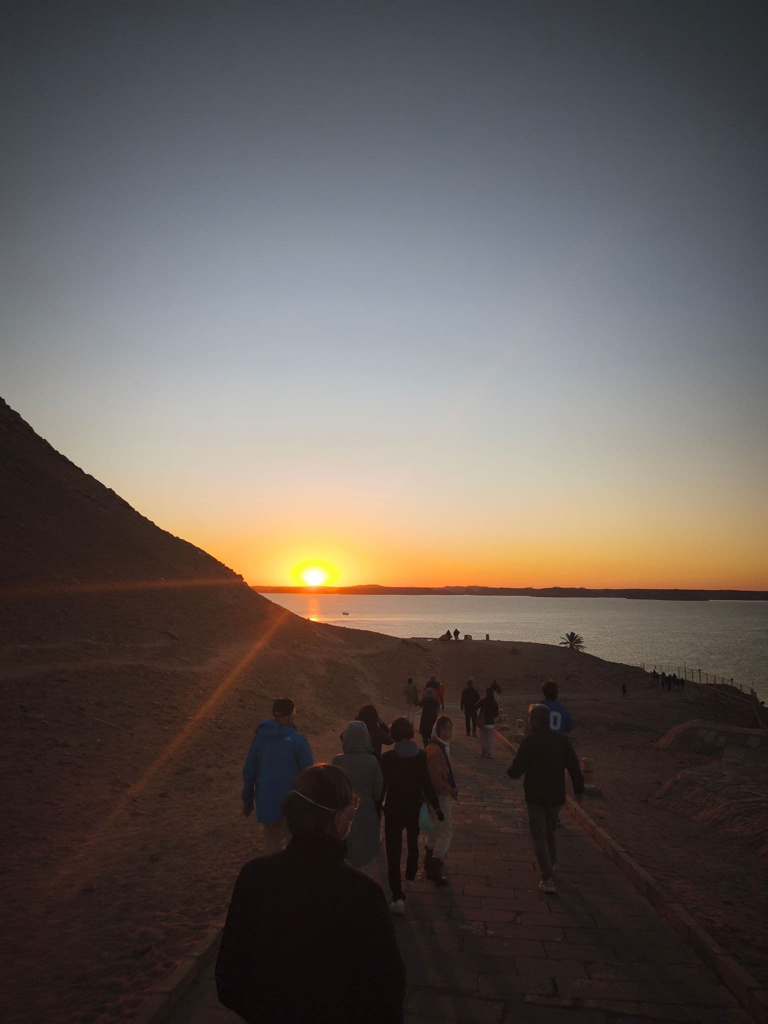 Abu Simbel approach at sunrise with a group of travelers walking a paved path toward Lake Nasser, Egypt.