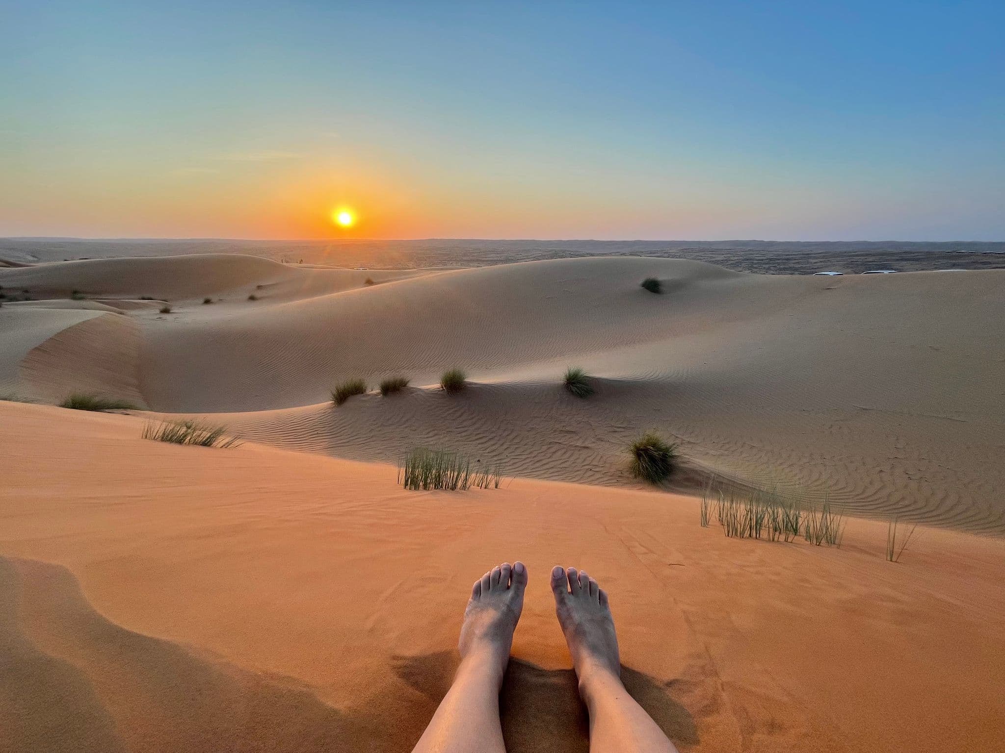 Sunset over rolling sand dunes with bare feet in the foreground, desert in the United Arab Emirates.