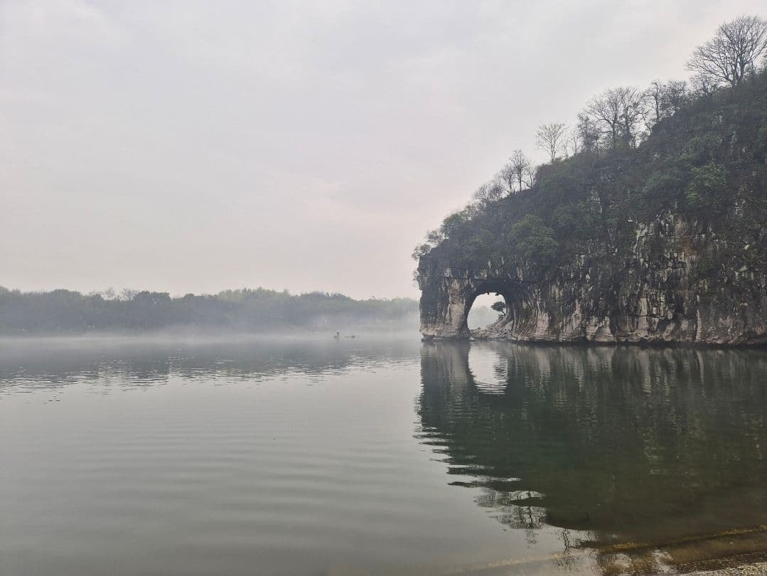 Elephant Trunk Hill rock arch rising from a misty Li River near Guilin, China, reflected in the calm water.