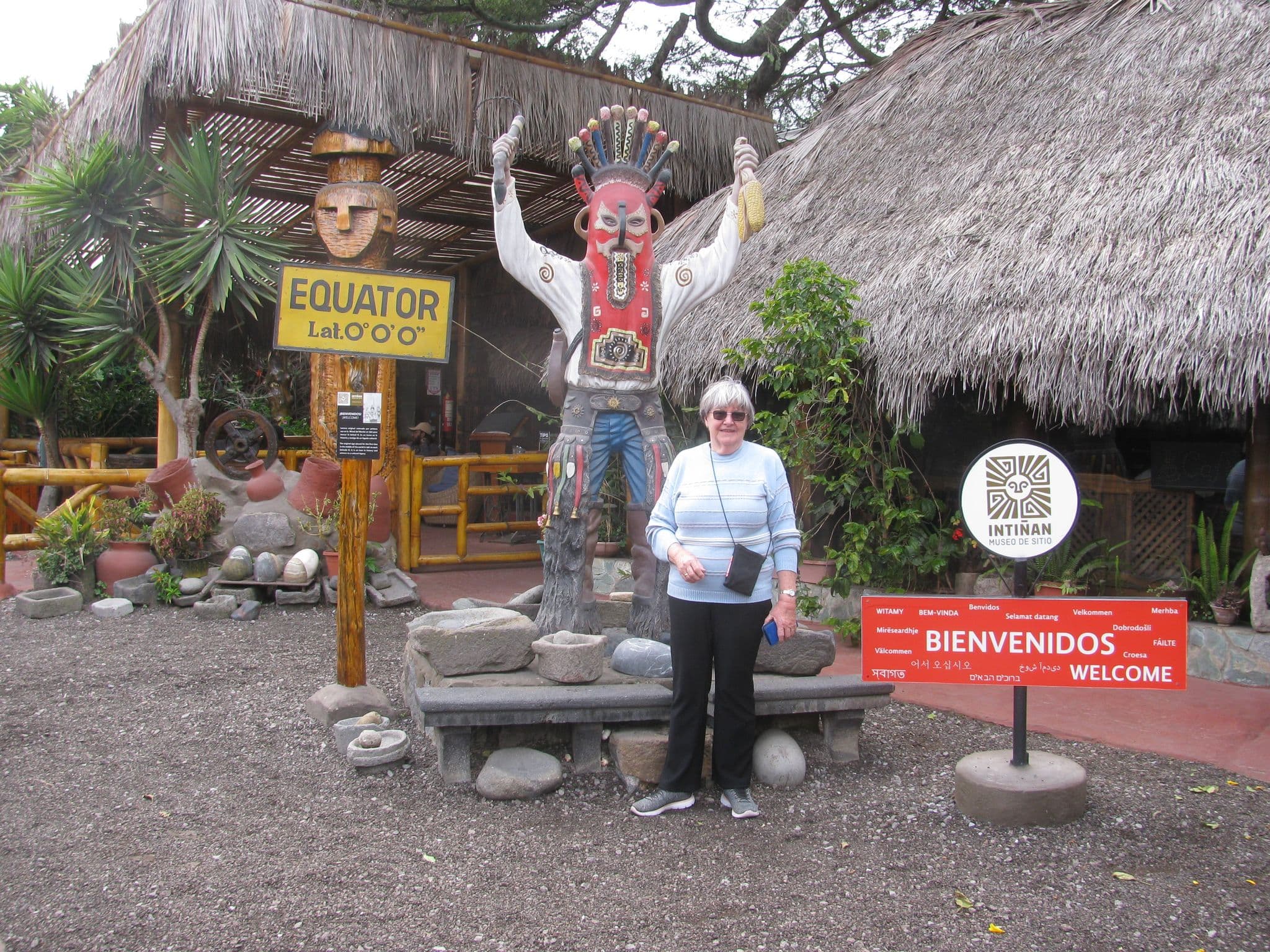 Equator sign and a visitor posing beside a ceremonial statue at Intiñan Museum, Quito, Ecuador.