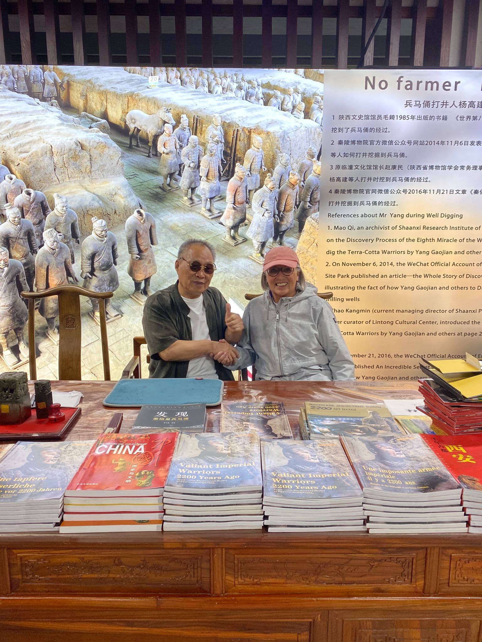 Terracotta Army mural behind two travelers shaking hands at a table stacked with guidebooks in Xi'an, China