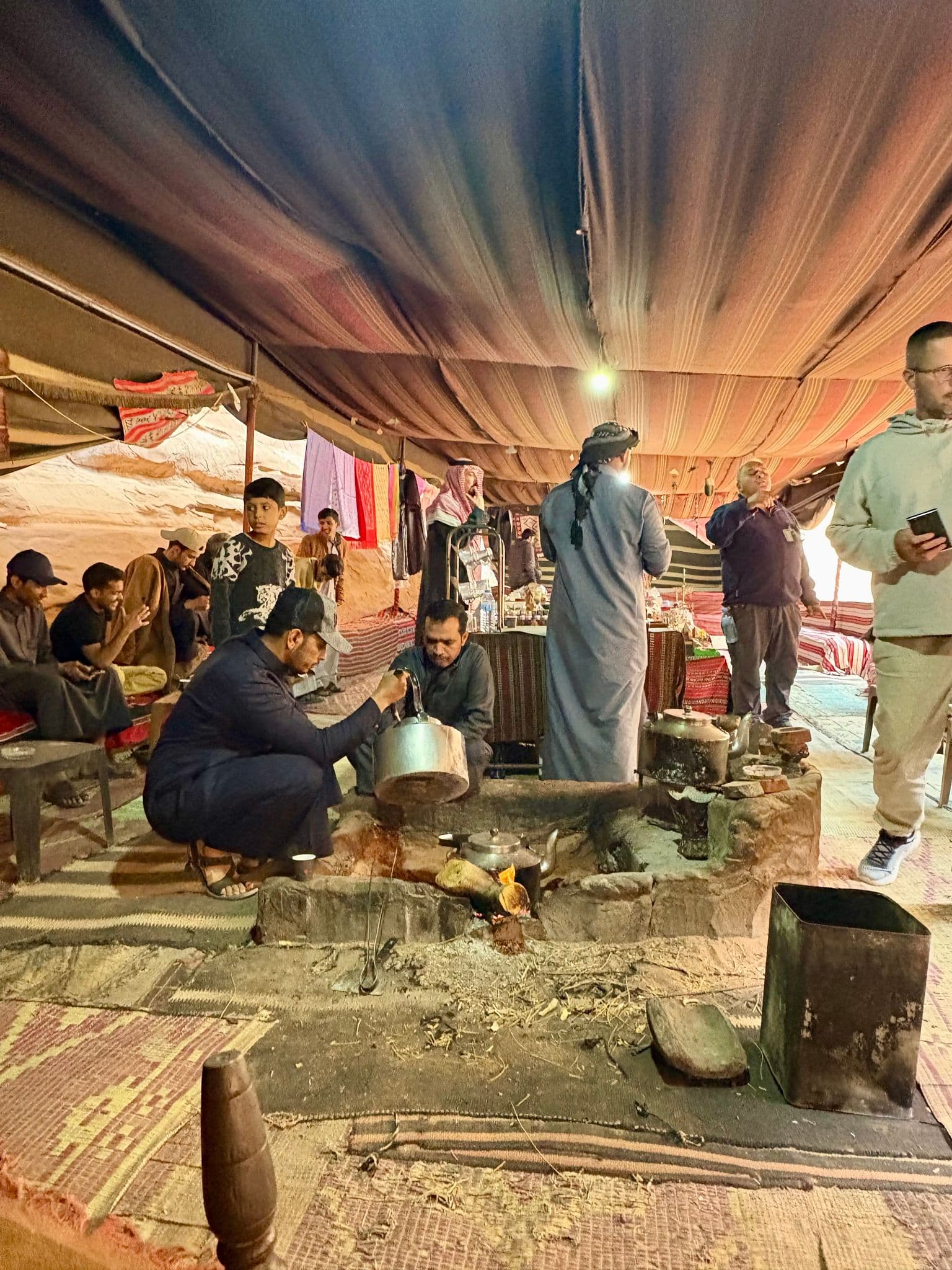 Men gathered inside a Bedouin tent around a cooking fire as one man pours tea, Wadi Rum, Jordan.