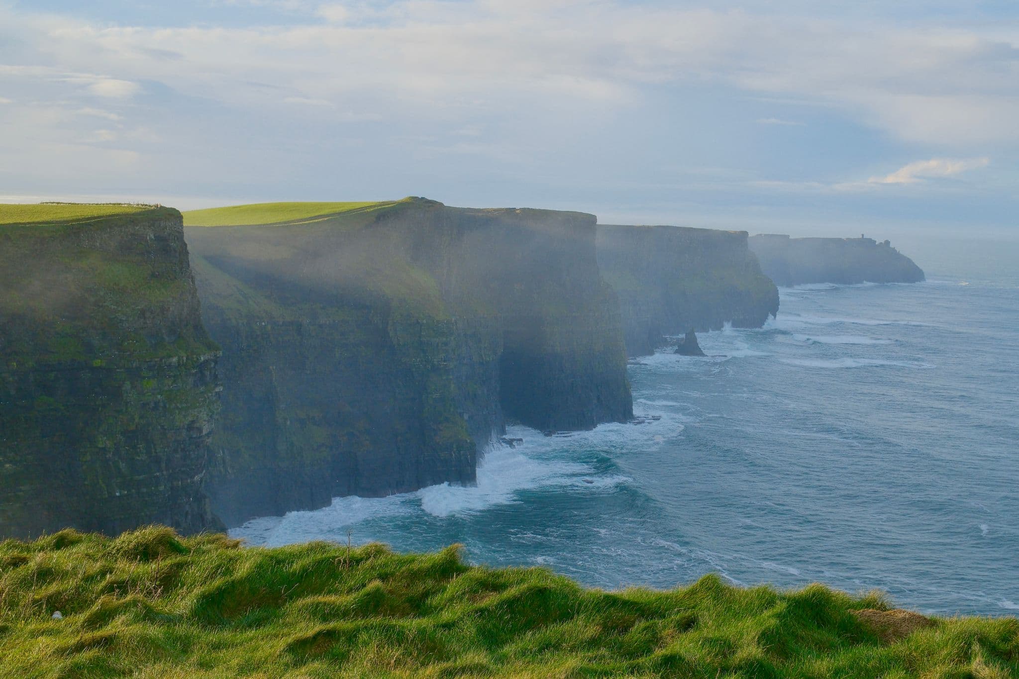 Cliffs of Moher rising above the Atlantic with waves below and grassy foreground, County Clare, Ireland.