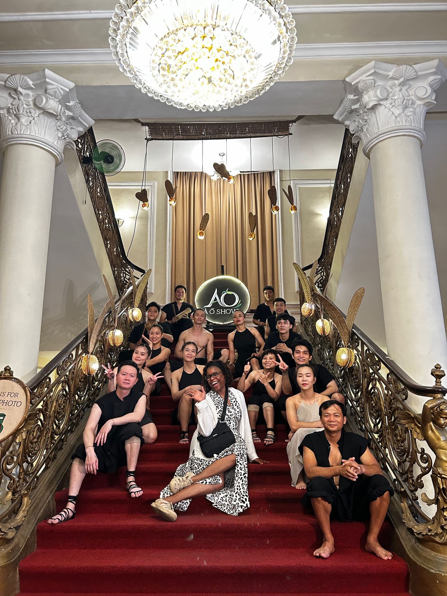 AO Show performers and a visitor posing on a grand red-carpeted staircase inside a theatre in Ho Chi Minh City, Vietnam.