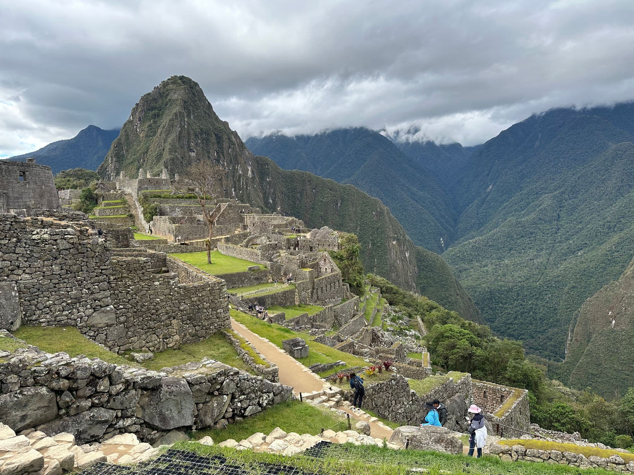 Machu Picchu ruins with Huayna Picchu behind, visitors walking stone terraces and paths, Cusco Region, Peru