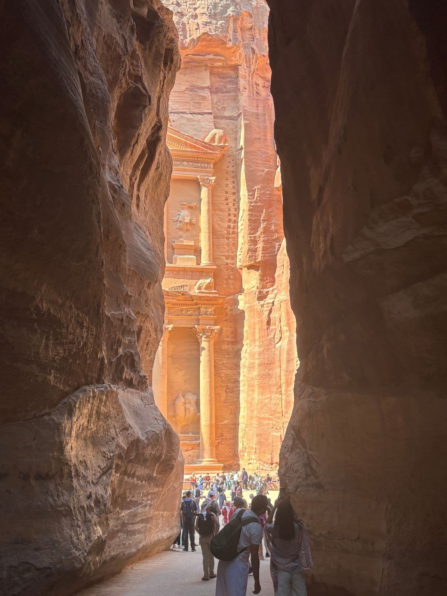 Al-Khazneh (the Treasury) at Petra framed by the Siq with tourists walking toward the carved façade, Jordan.