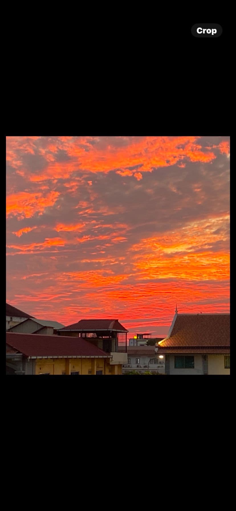Vivid orange and red sunset clouds over hotel rooftops and a temple-style roof in Cambodia.