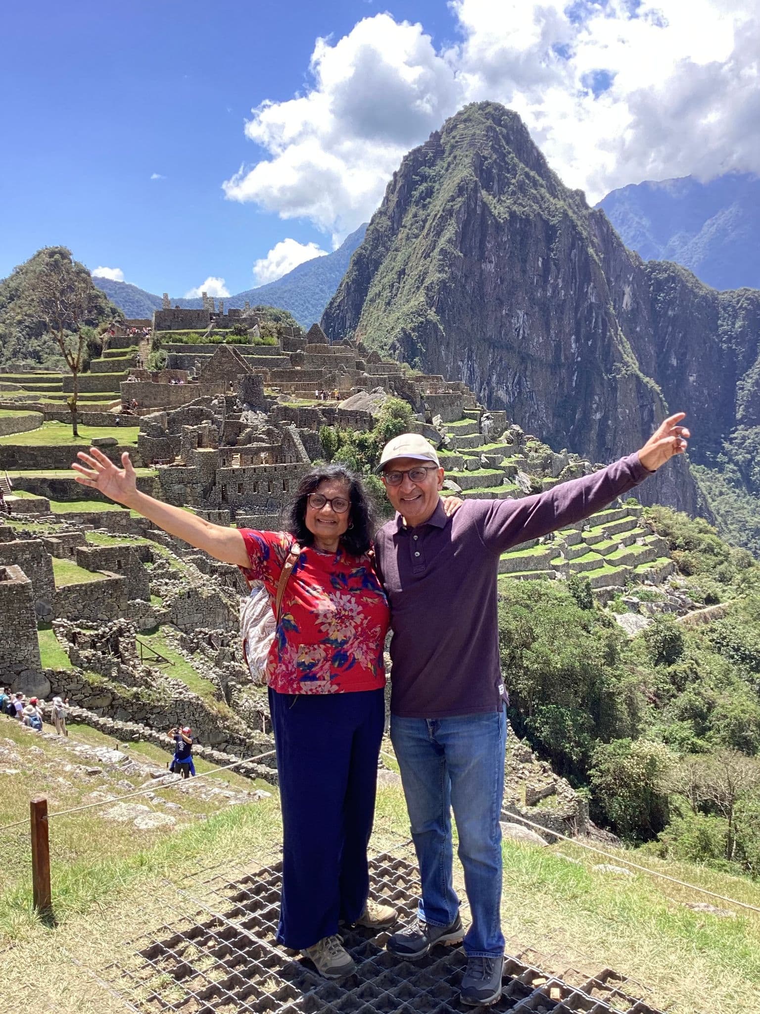 Machu Picchu ruins with Huayna Picchu behind and two travelers posing with arms outstretched, Cusco Region, Peru