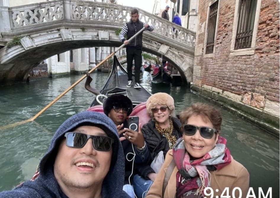 Gondola with four travelers and a gondolier passing under a small stone bridge on a Venice canal, Venice, Italy.