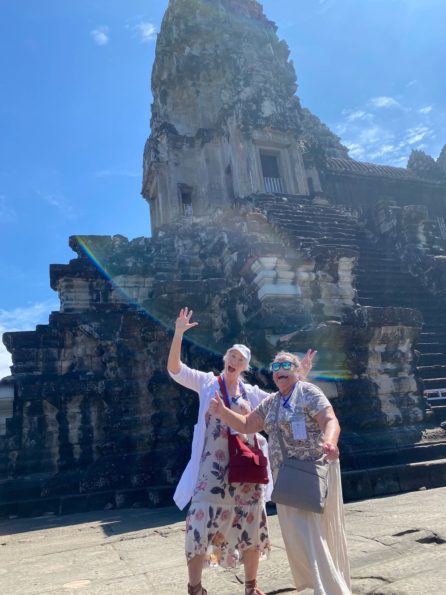 Angkor Wat temple with two women posing and waving in front during a sunny tour, Siem Reap, Cambodia.