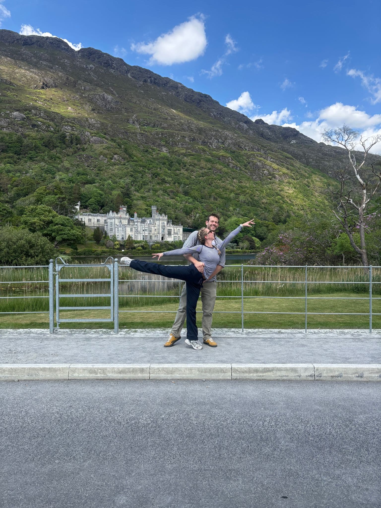 Kylemore Abbey with a couple striking a ballet lift on a lakeside path, Connemara, County Galway, Ireland.