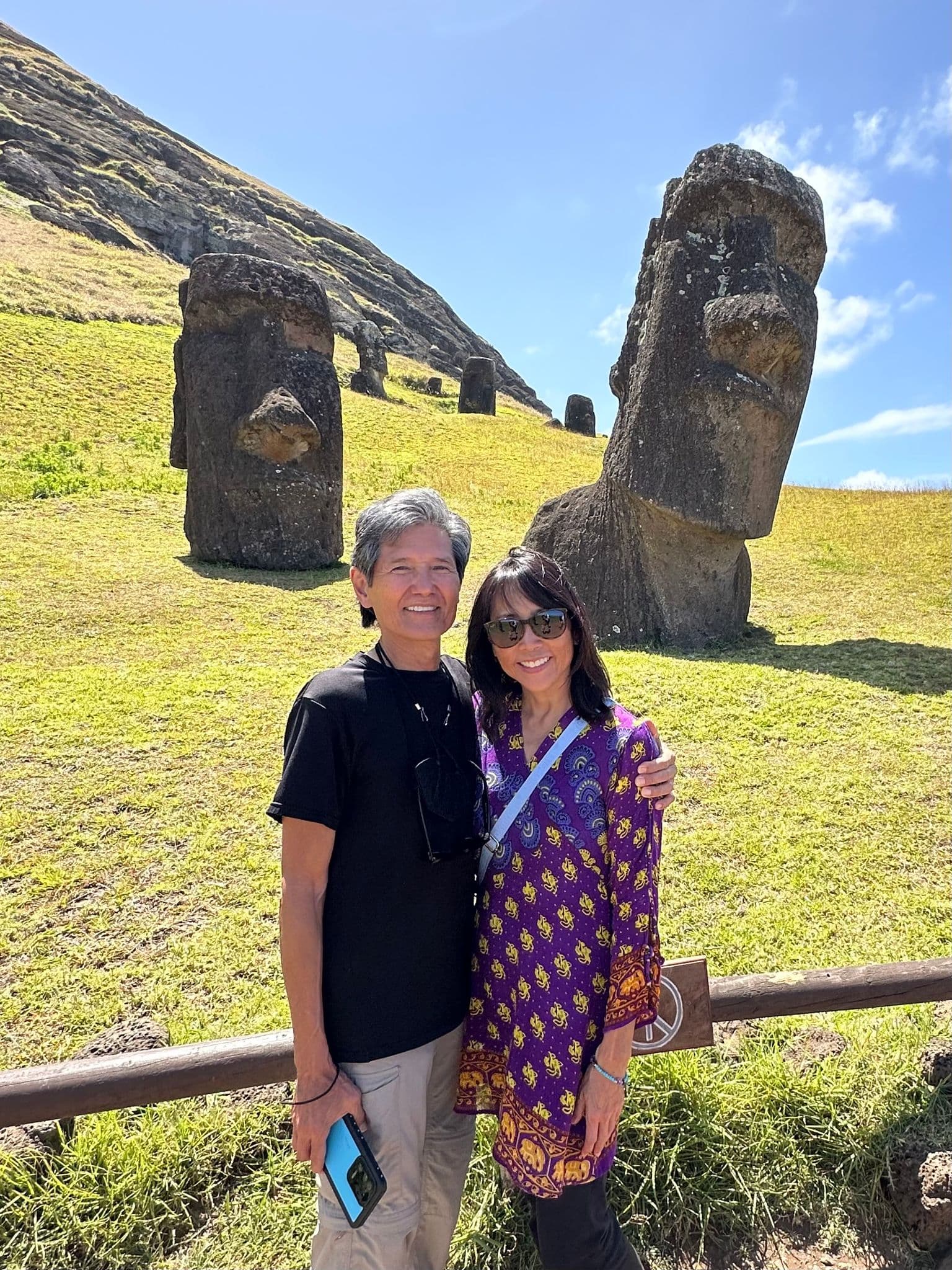 Moai statues at Rano Raraku with two travelers posing in front on a sunny hillside, Easter Island, Chile.