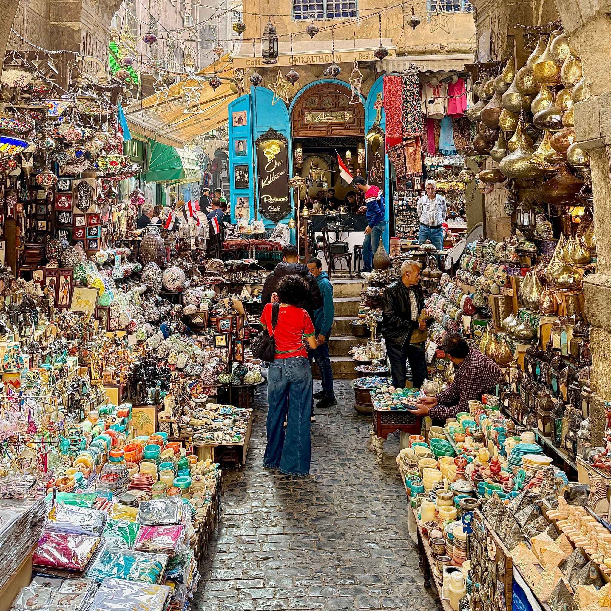 Khan el-Khalili bazaar alley in Cairo, Egypt, with shoppers browsing colorful lanterns, pottery, and brassware among crowded stalls.