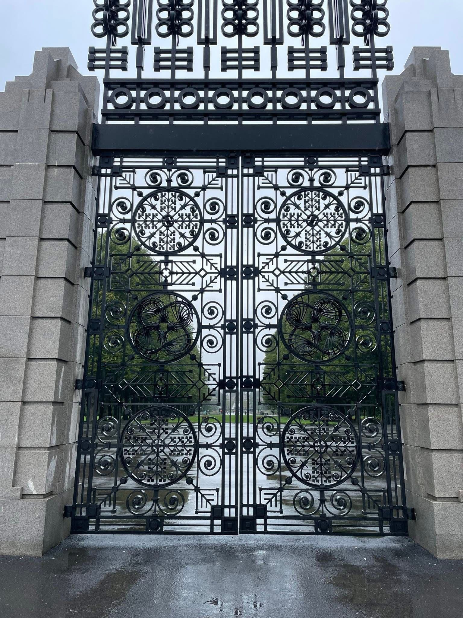 Ornate black wrought-iron entrance gate to Frogner Park (Vigeland Sculpture Park) in Oslo, Norway, framing a tree-lined path