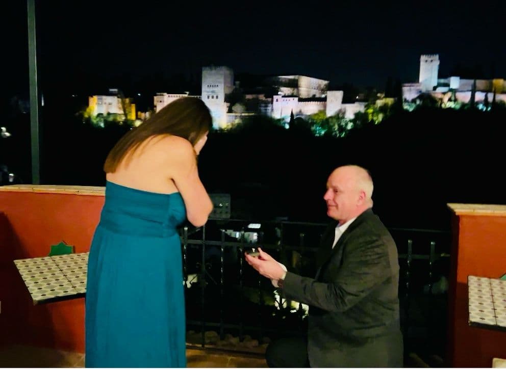 La Alhambra lit at night with a man proposing on a balcony and a woman covering her face, Granada, Spain.