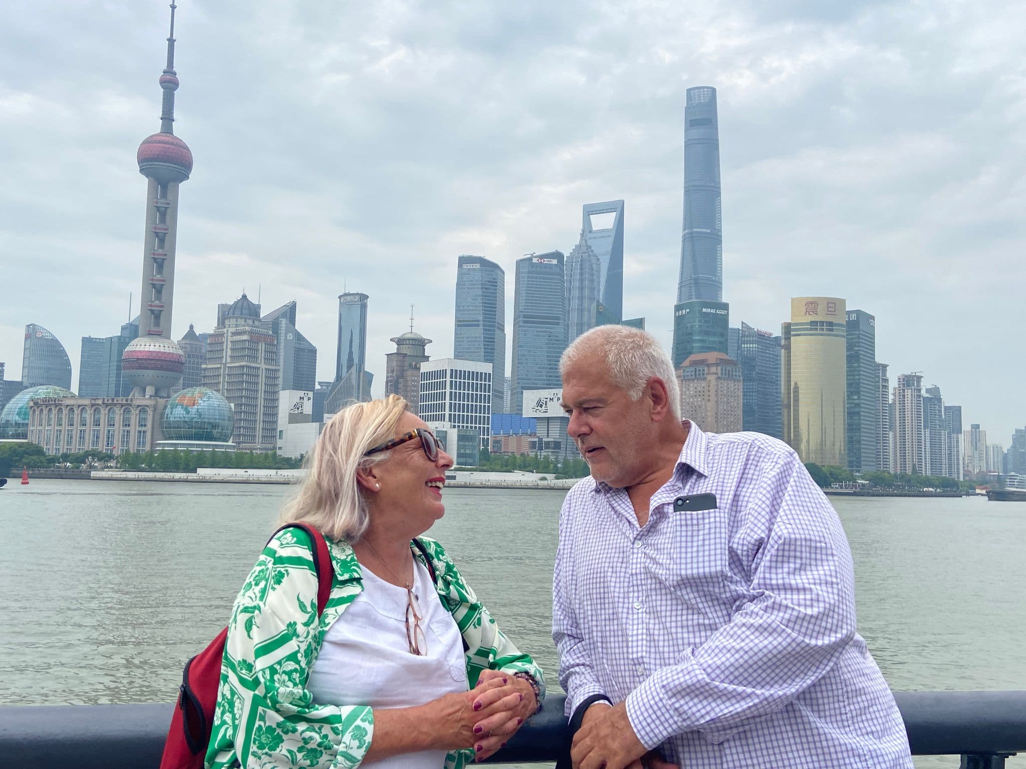 Oriental Pearl Tower and Pudong skyline behind two travelers chatting on the Bund, Shanghai, China