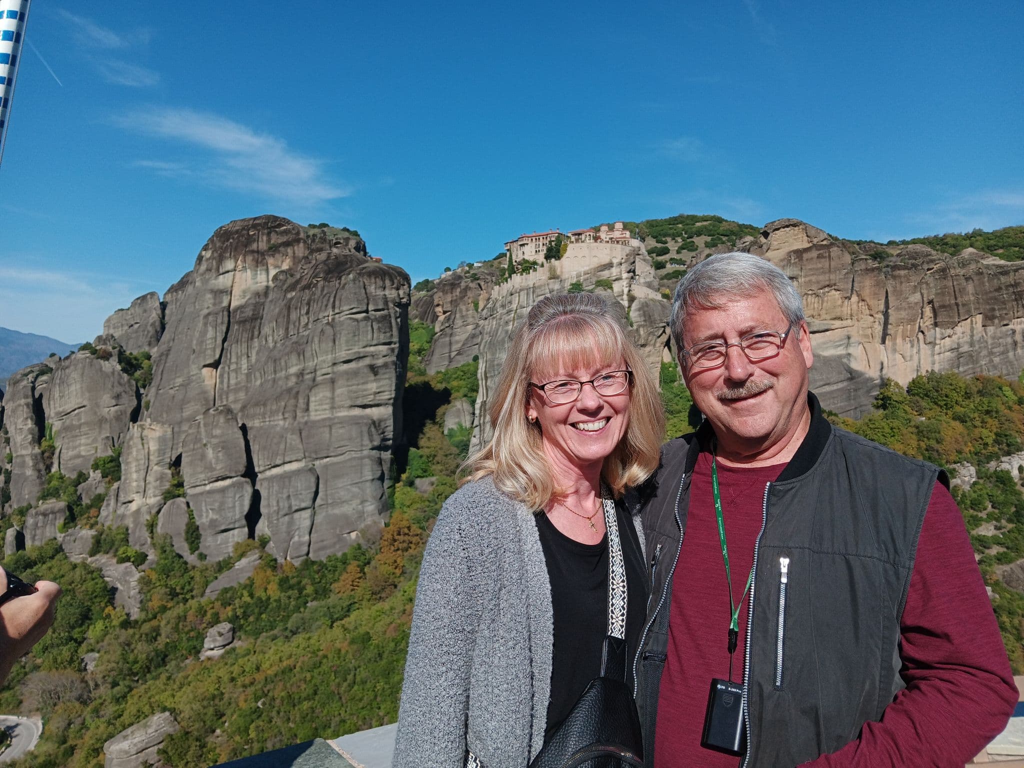 Meteora rock cliffs and cliffside monastery with a smiling couple posing on a viewpoint, Meteora, Greece.