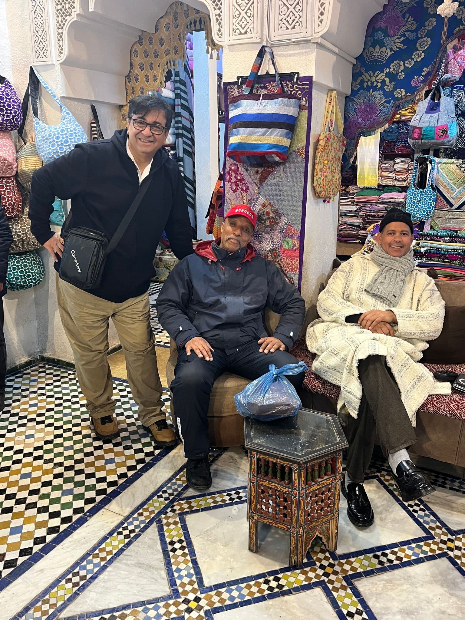 Three men sitting in a colorful textile stall in the Fez medina bazaar, Fes, Morocco.
