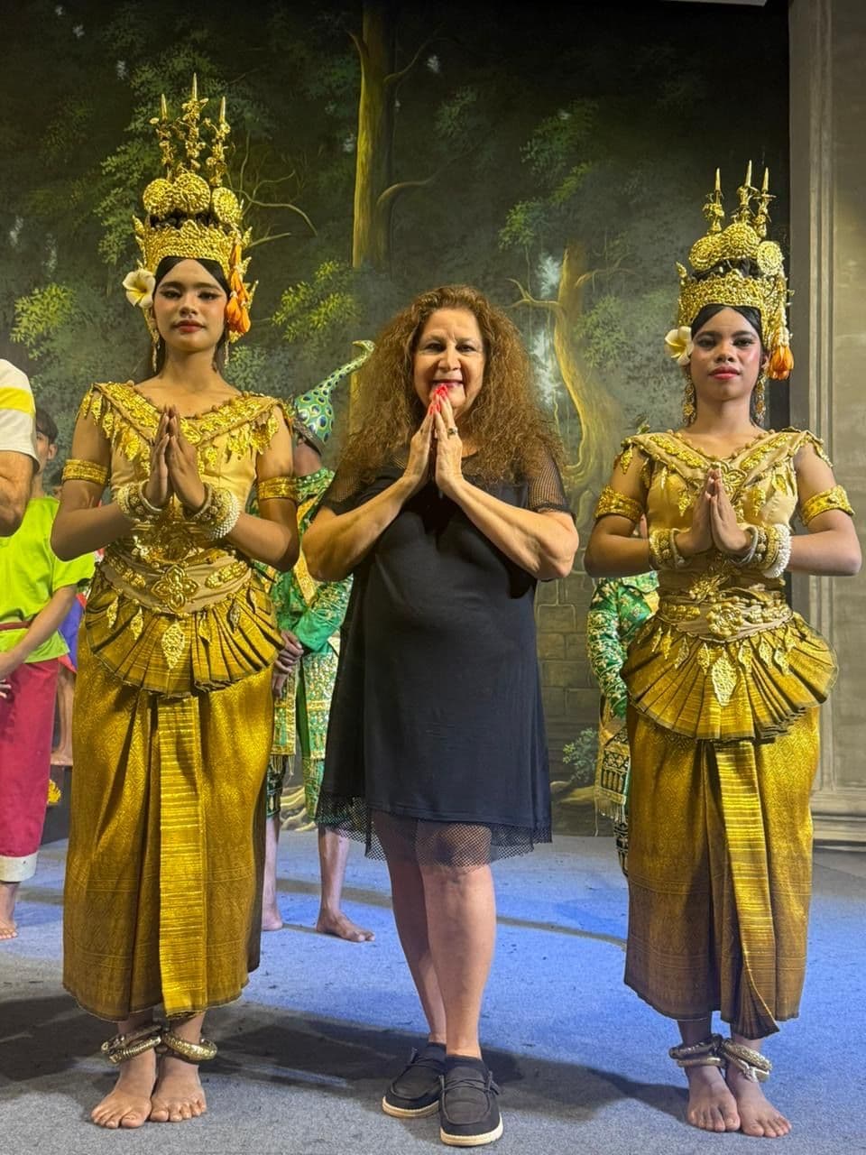 Two Apsara dancers flanking a traveler, all with hands pressed together during a cultural show in Siem Reap, Cambodia.