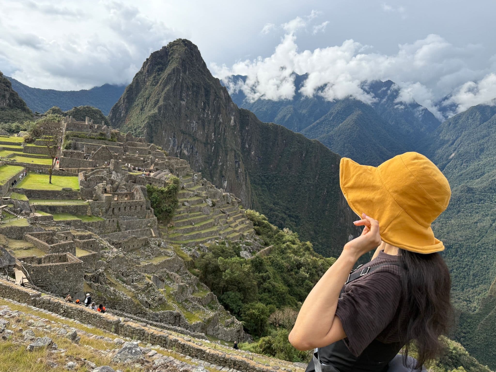 Machu Picchu ruins and Huayna Picchu peak with a person in a yellow hat looking over the stone terraces in Peru