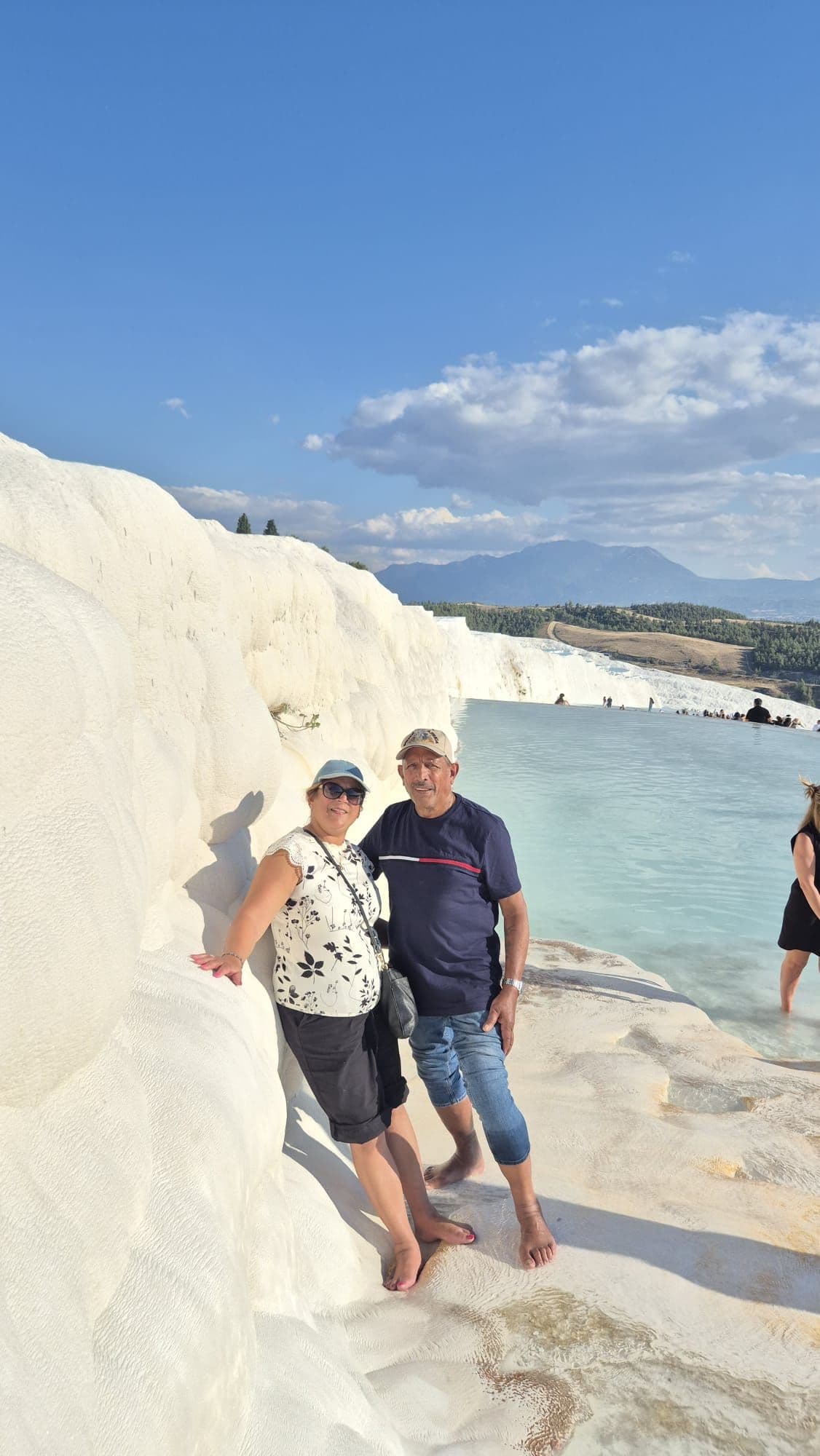 Pamukkale travertine terraces and a shallow thermal pool with two barefoot travelers standing at the edge, Denizli Province, Turkey.