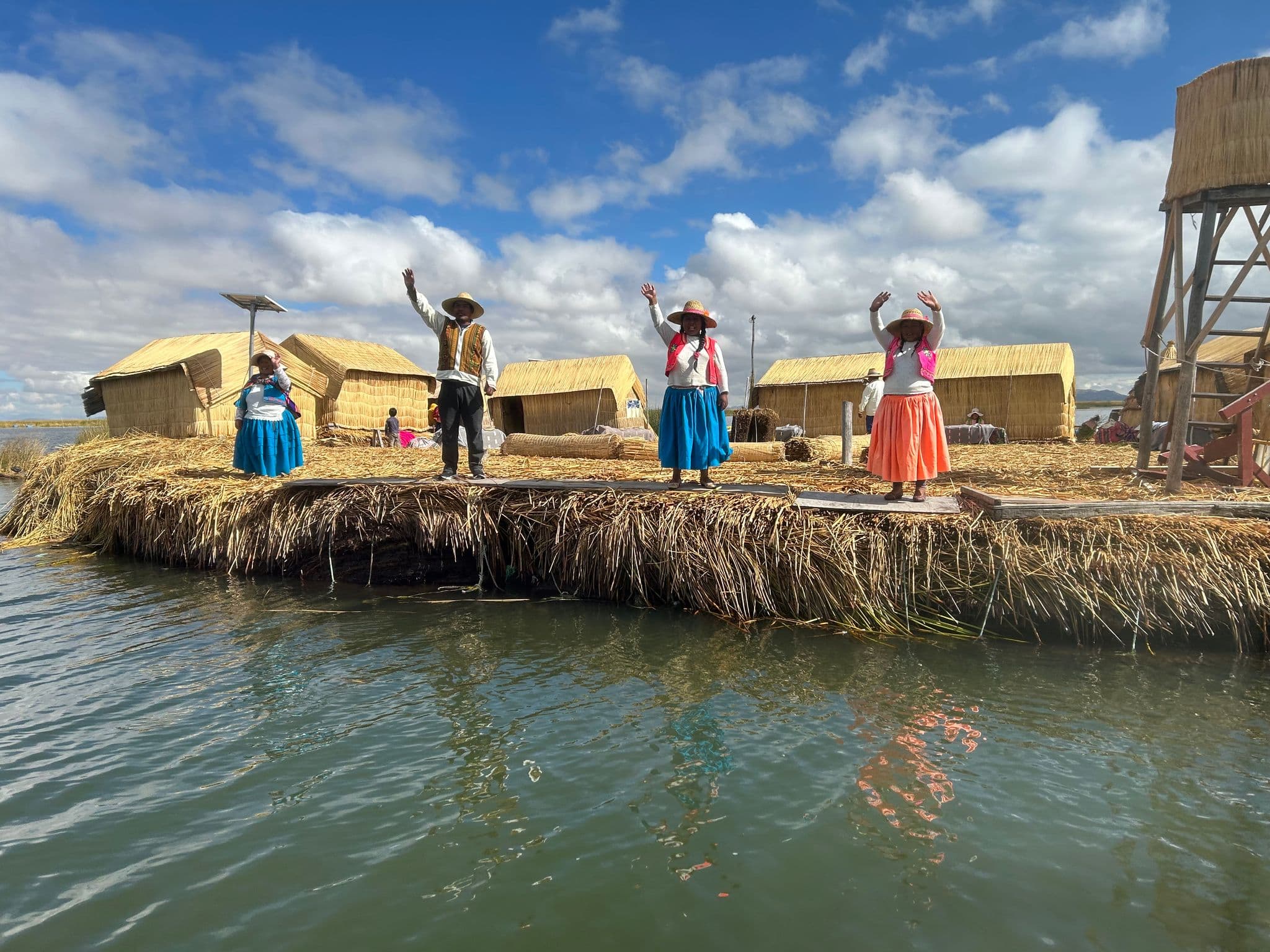 Uros floating island on Lake Titicaca with locals in traditional dress standing and waving beside reed huts, Peru.
