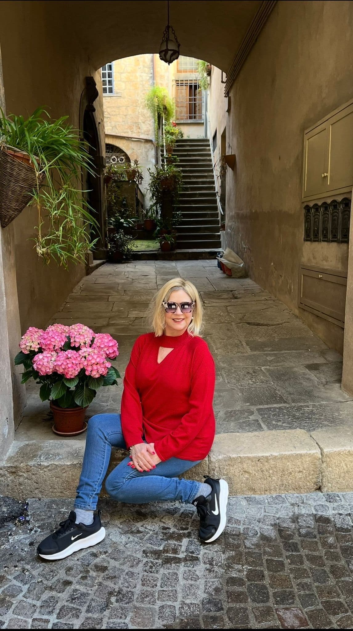 Woman sitting on a stone step in an arched passageway with pink hydrangeas and stone stairs behind her in Oliveto, Italy.
