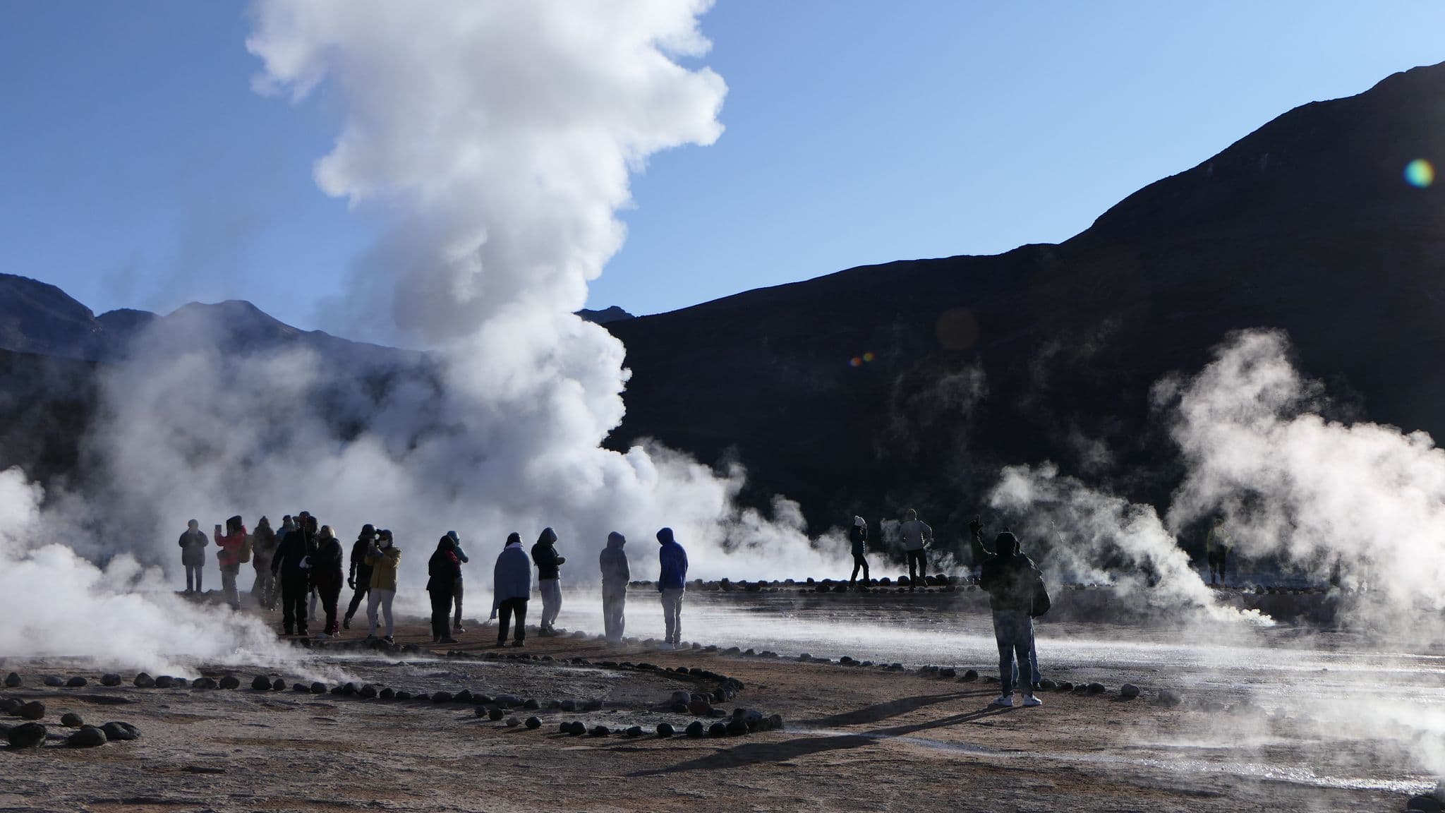 Steam plumes rising from geothermal geysers as tourists photograph the scene at El Tatio Geysers, Chile.
