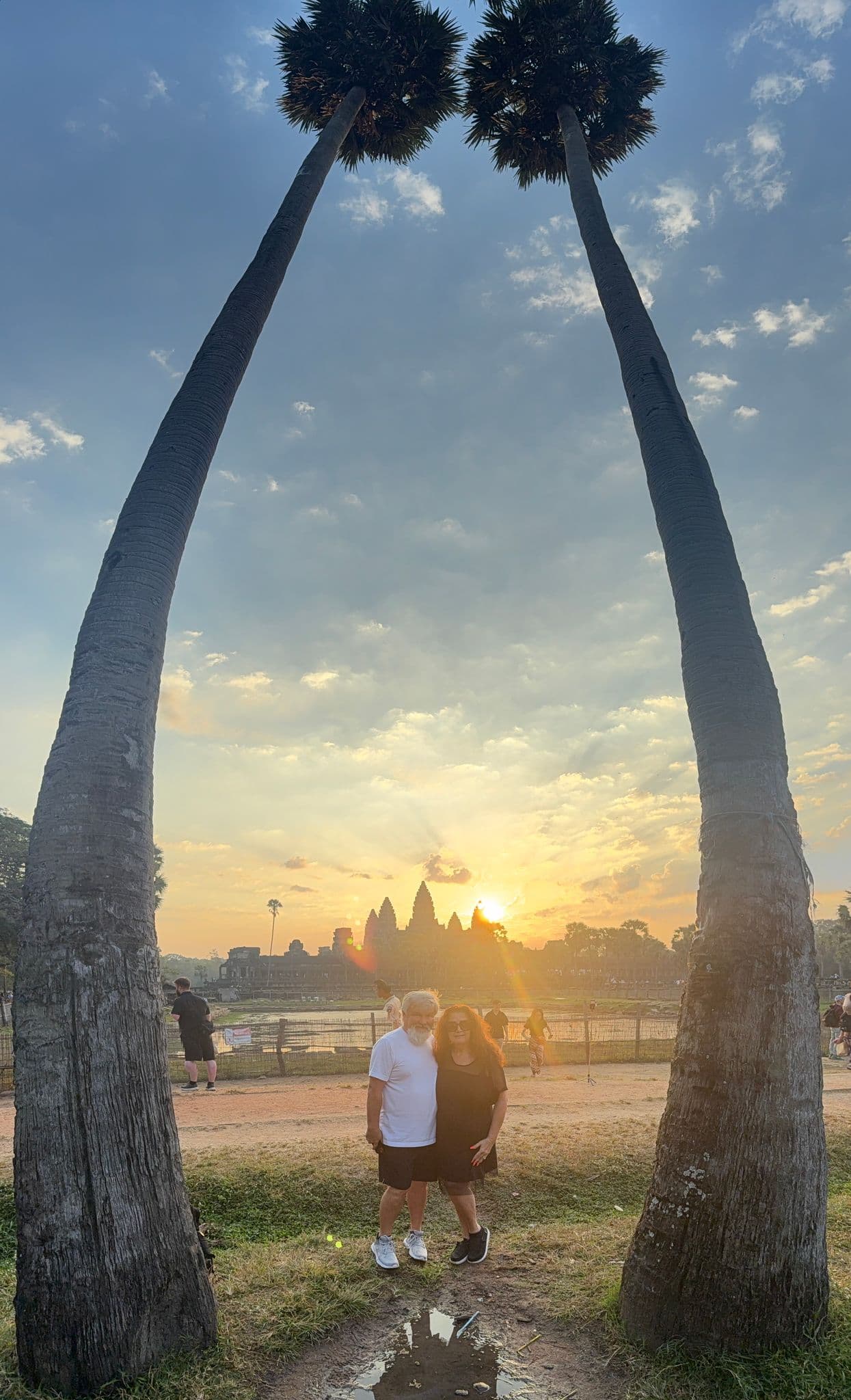 Angkor Wat temple at sunrise with a couple posing between two tall palm trees, Siem Reap, Cambodia.