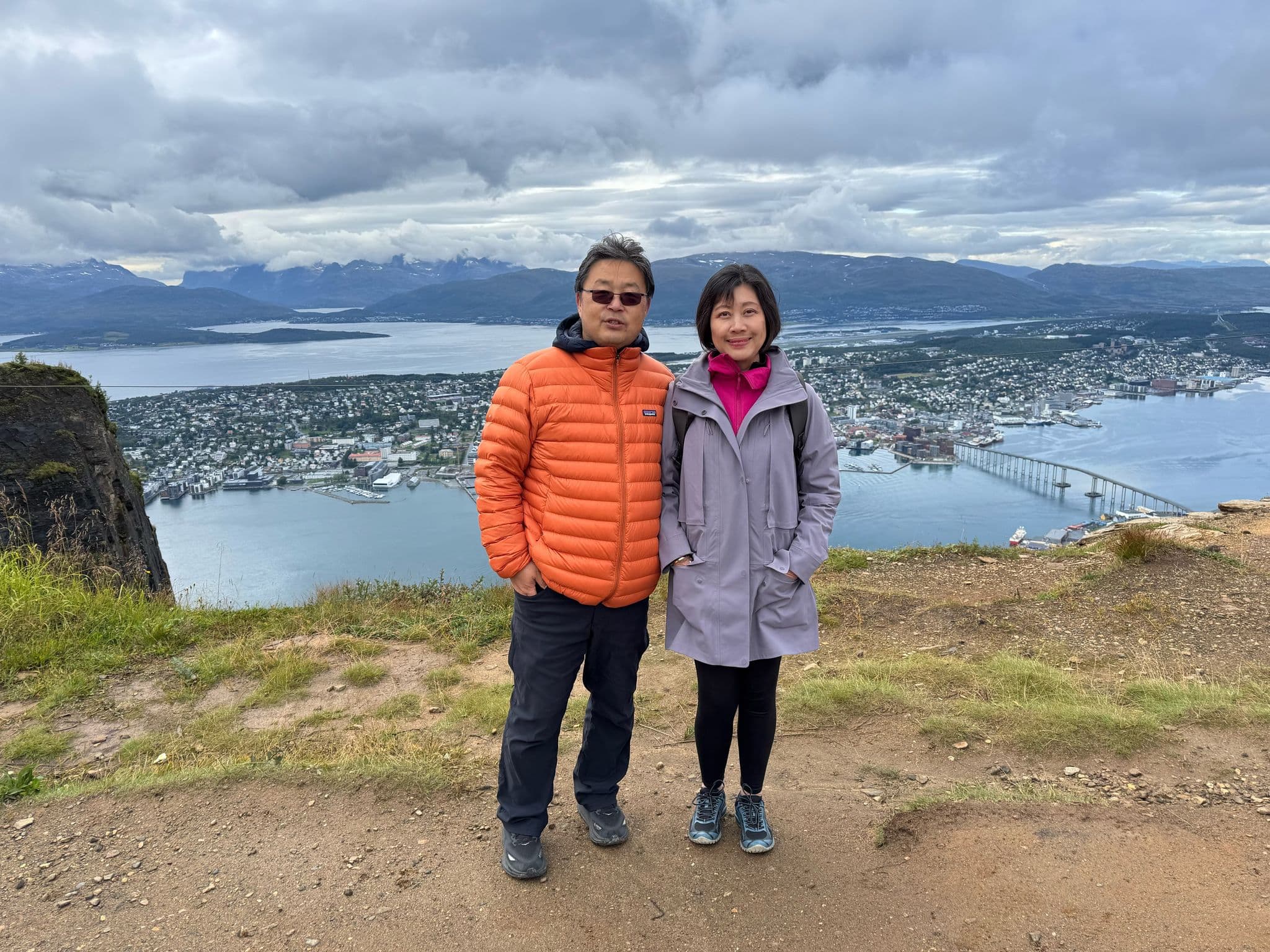 Tromsø and the Tromsø Bridge seen from a hillside viewpoint, with two travelers standing in the foreground, Tromsø, Norway.