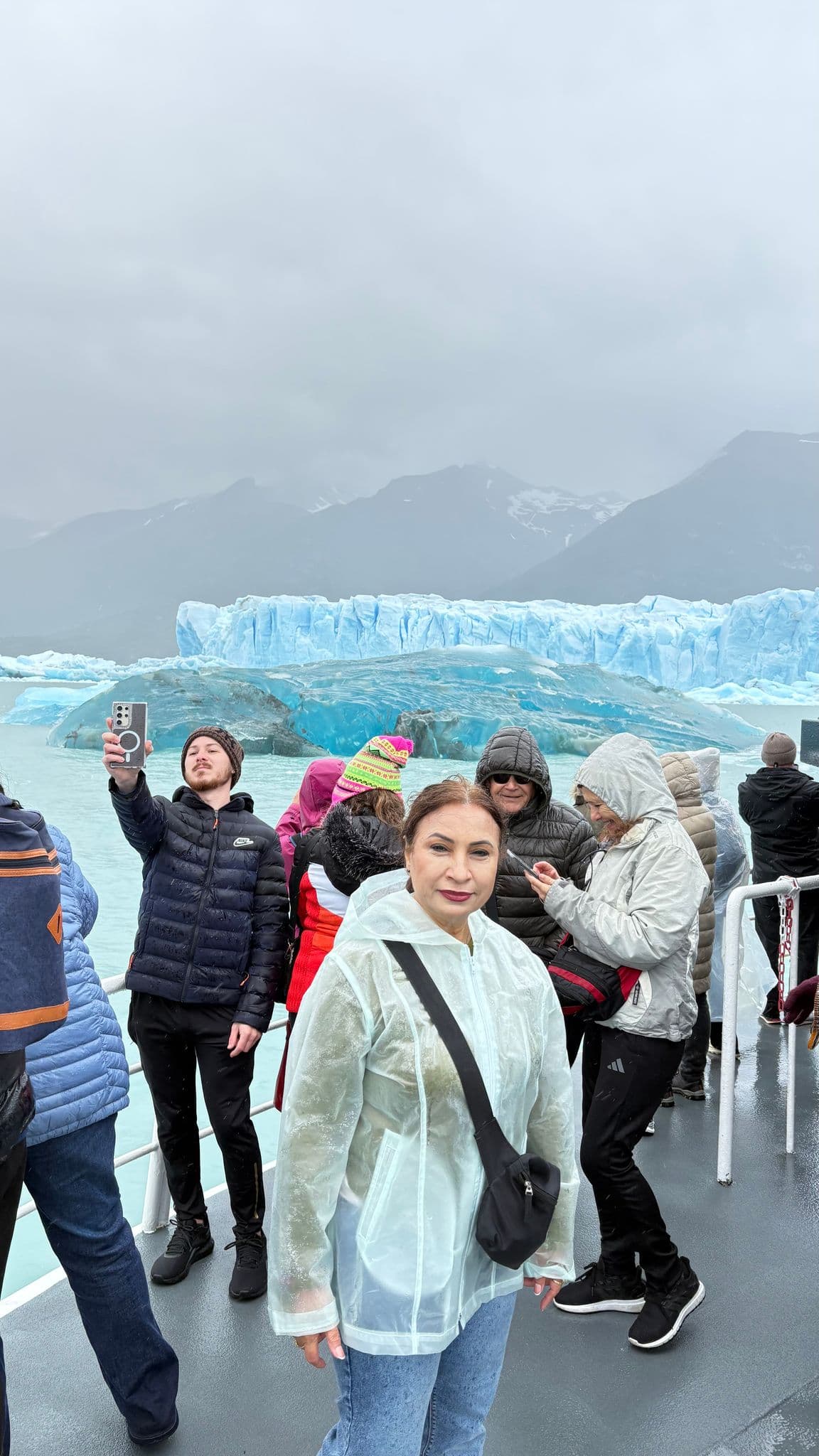 Perito Moreno Glacier's blue ice behind tourists on a boat; woman in a raincoat in foreground, Santa Cruz, Argentina.