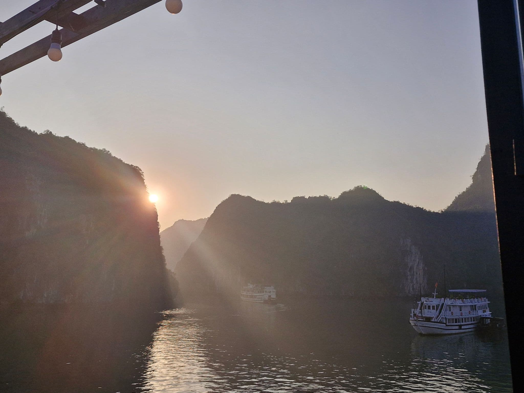 Sun setting between limestone karsts with tour boats on Ha Long Bay, Vietnam.